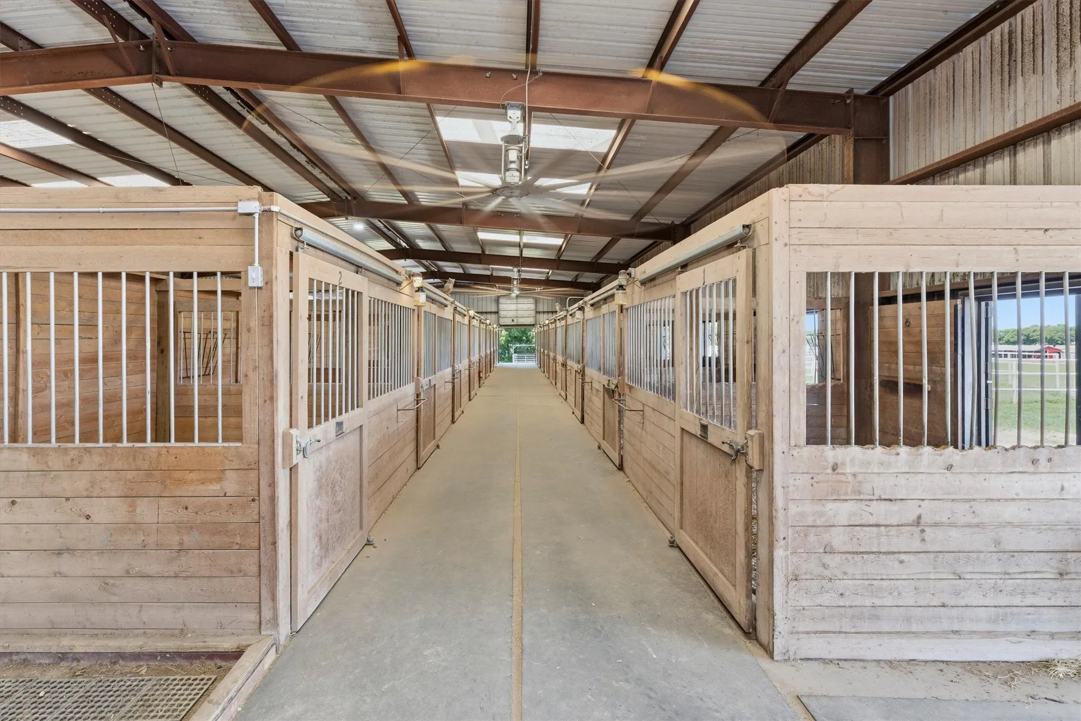 18 Stall show barn featuring wood-paneled stalls with metal grates, a concrete aisle, overhead lighting, and large ceiling fans