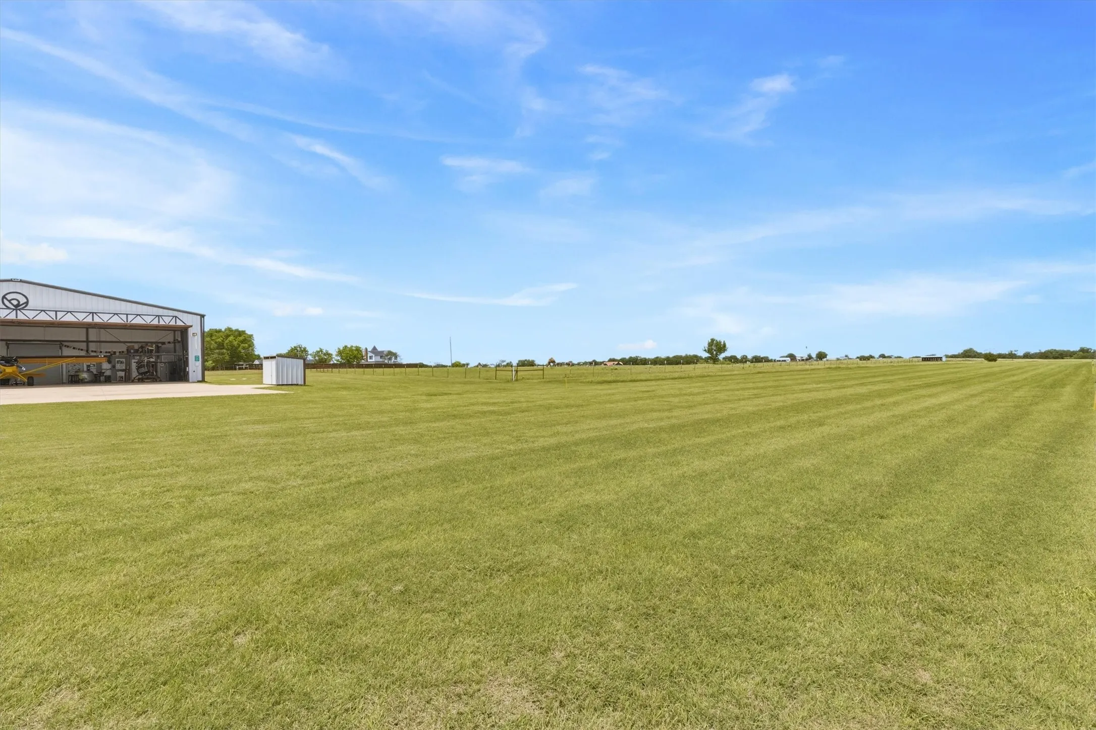 Expansive green field with a large metal-clad hangar featuring an open bay and a concrete apron