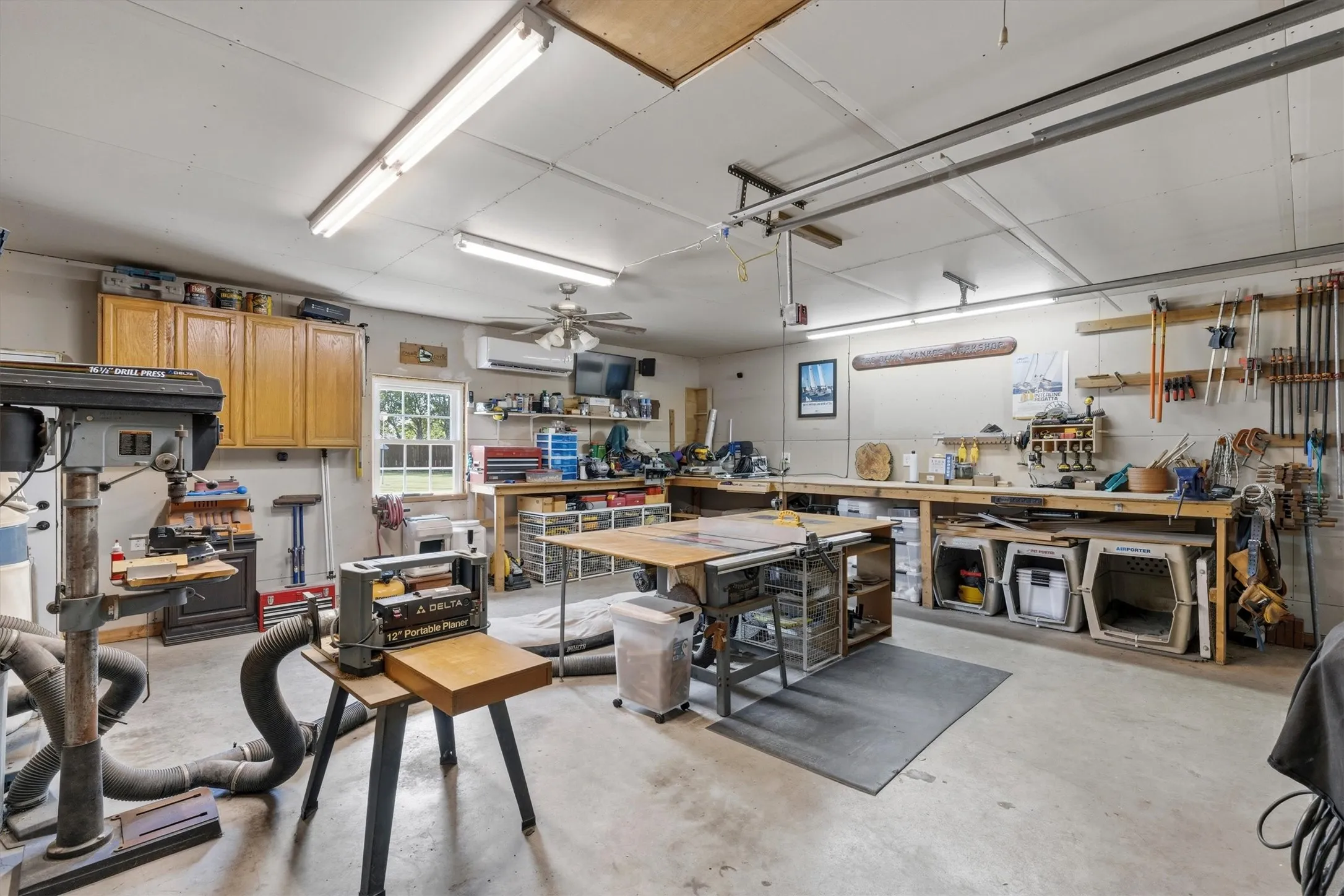 Spacious garage workshop featuring concrete flooring, extensive built-in shelving, ample overhead lighting, a ceiling fan, and a window for natural light