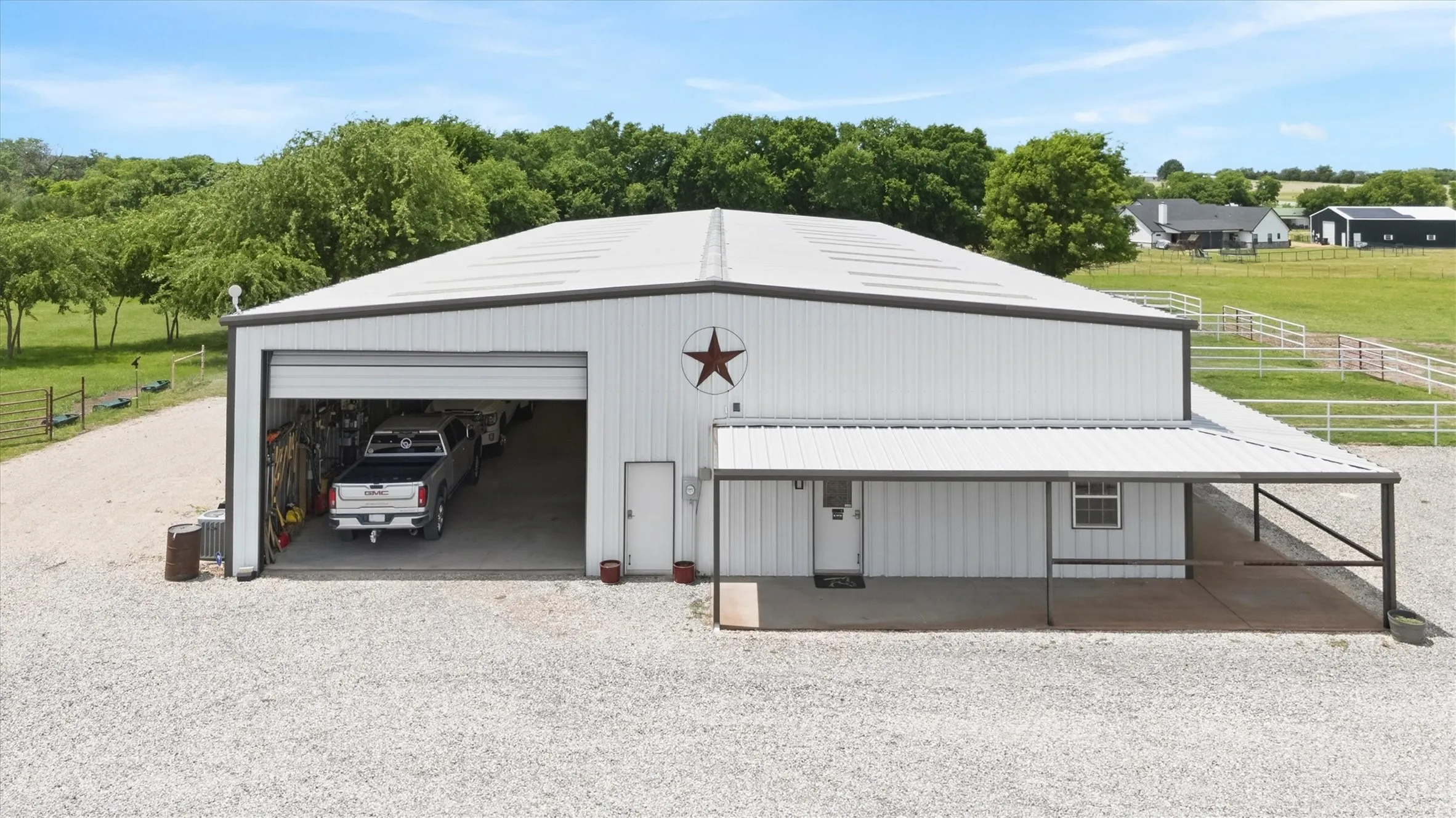 White metal building with a large roll-up garage door, an attached covered patio, and a gravel driveway
