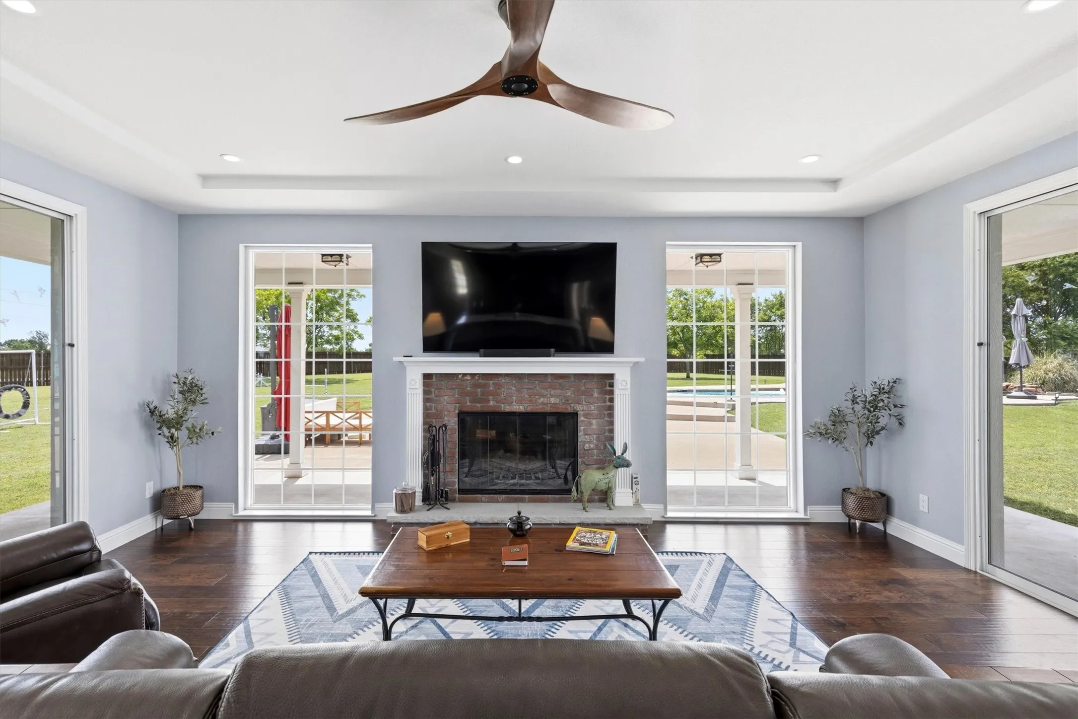 Living area featuring wood-finish flooring, a brick fireplace with a white mantel, a tray ceiling, and recessed lighting