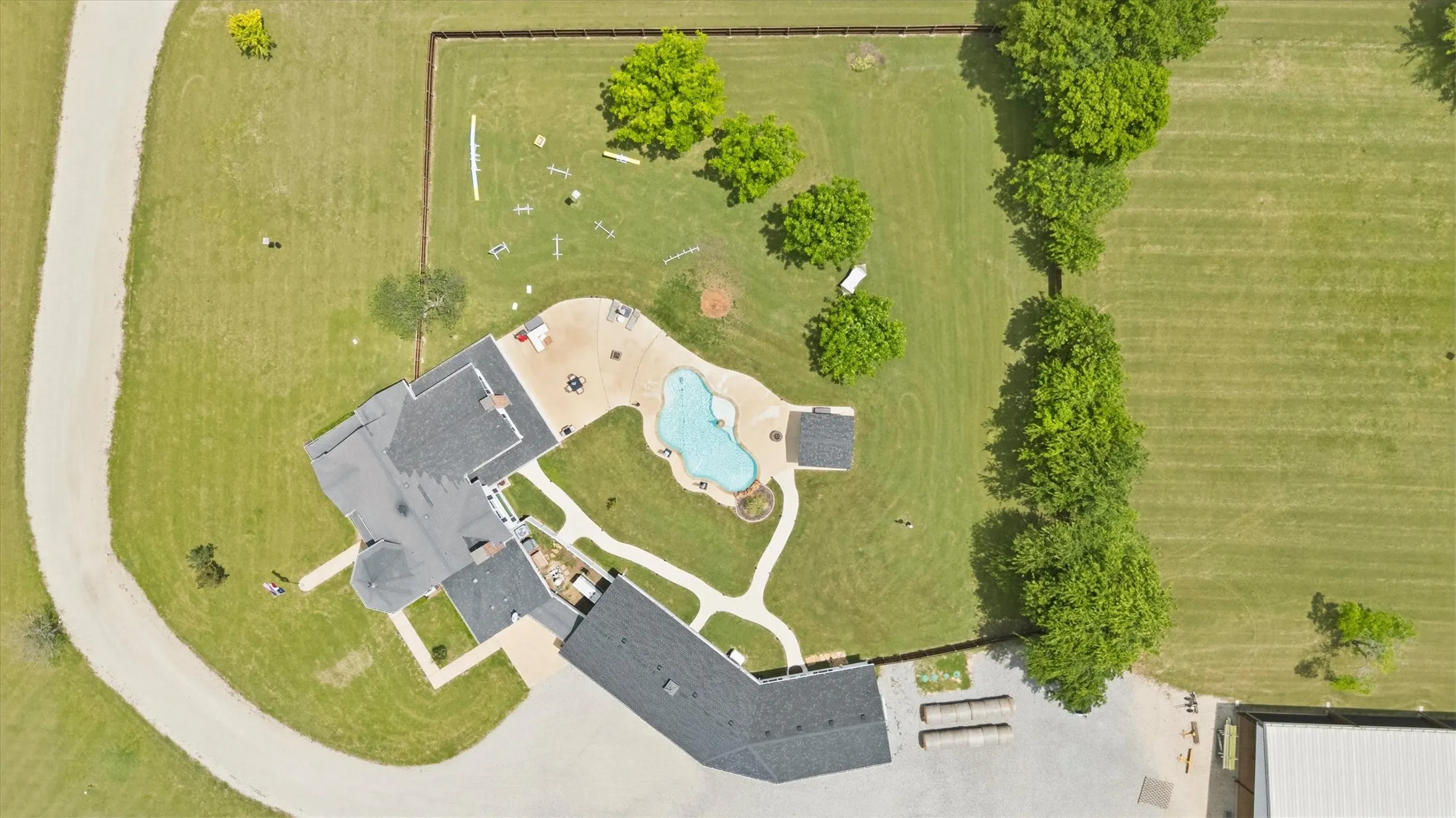 Expansive property featuring a curved driveway, large manicured lawn, and a custom-shaped swimming pool with surrounding hardscaping