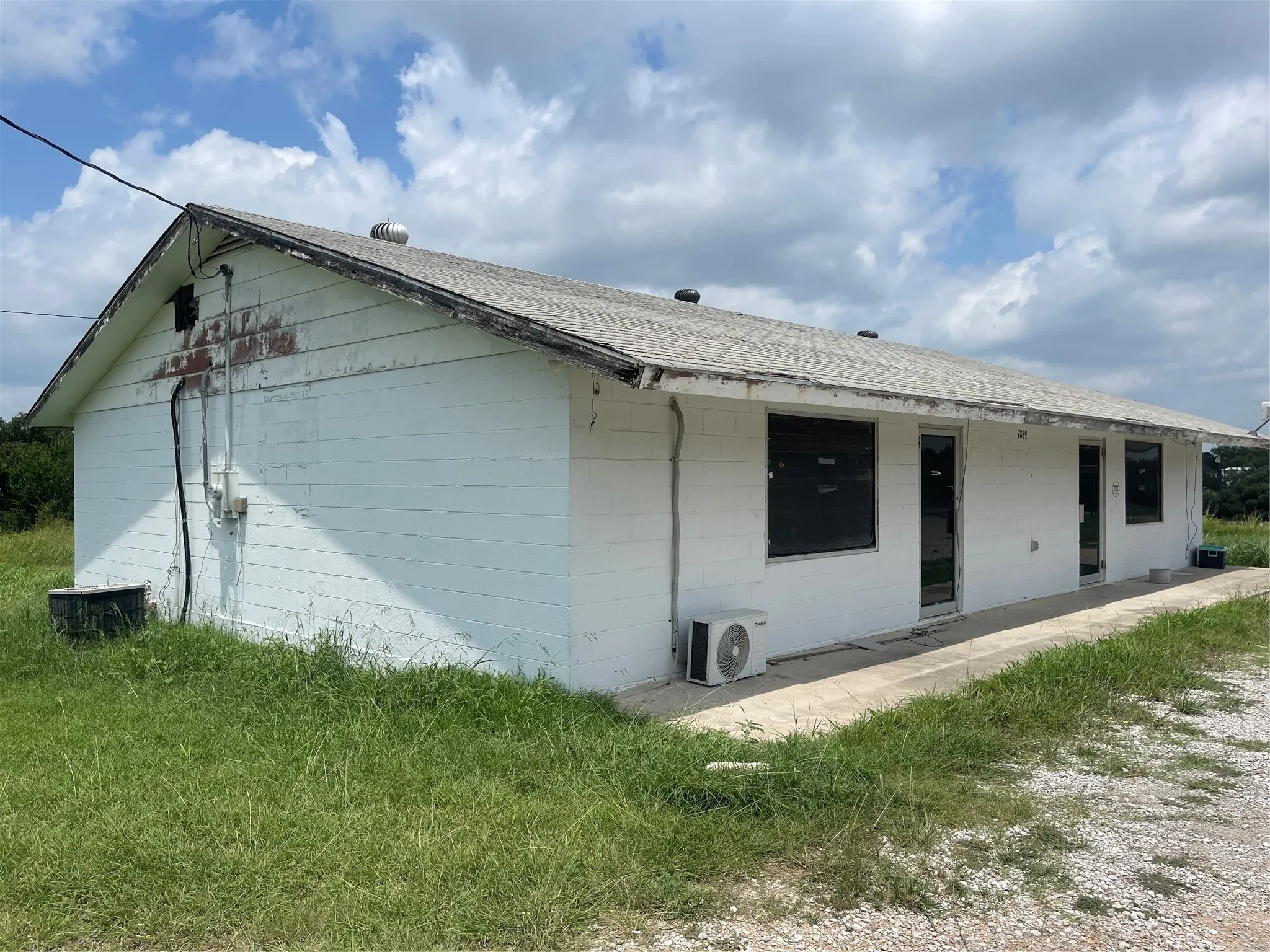Front view of building featuring a shingled roof, a patio, and concrete block siding