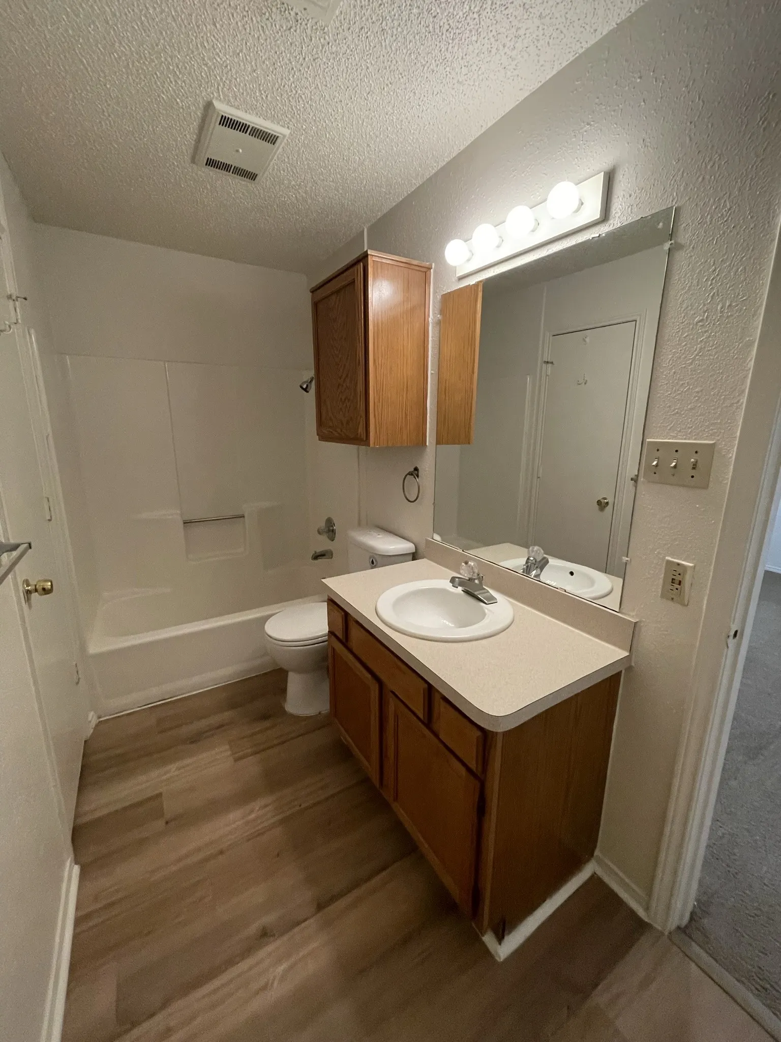 Wood-finish flooring with a white bathtub, toilet, and a vanity featuring an integrated sink, laminate countertop, and wood-toned cabinetry