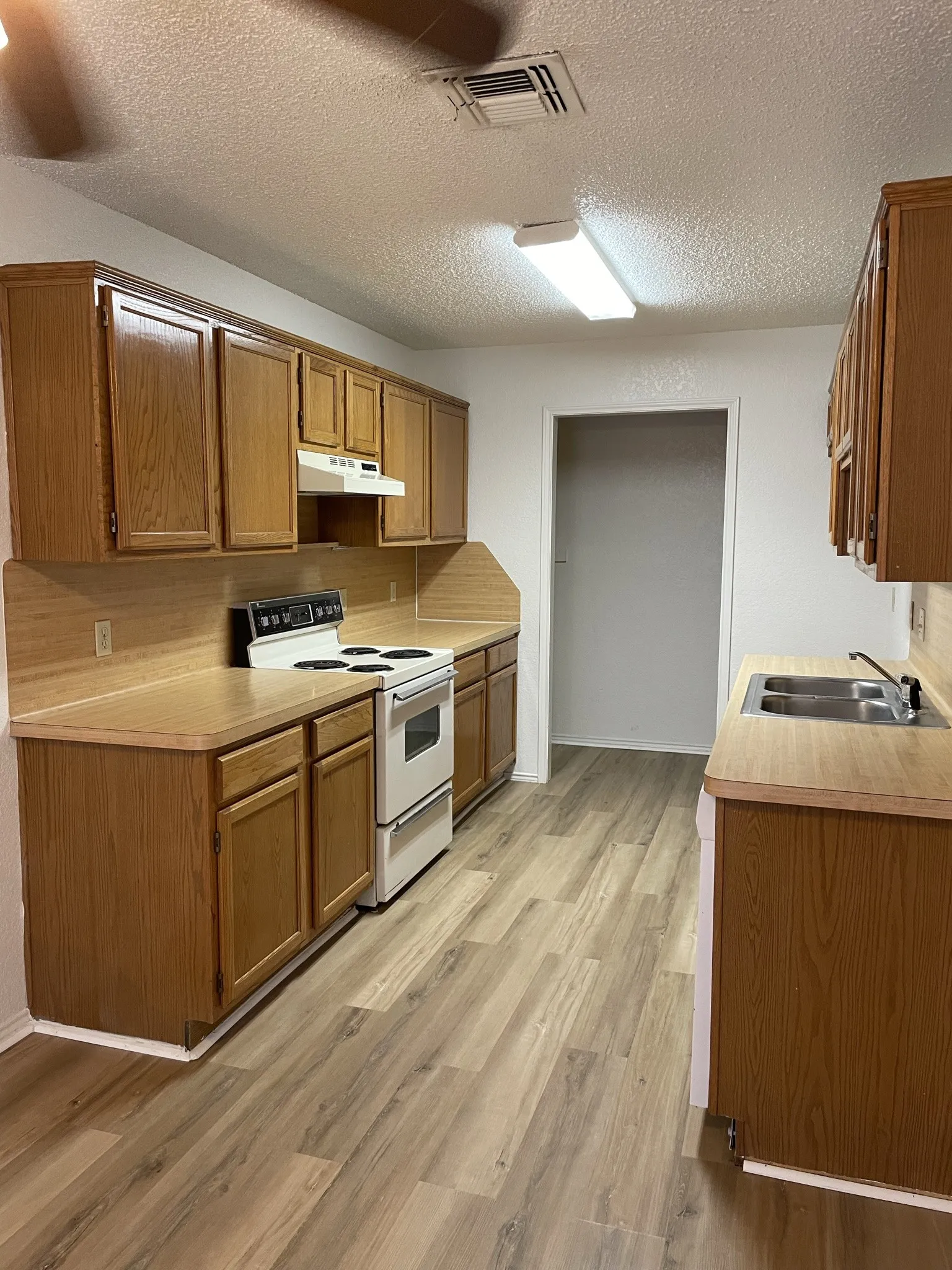 Kitchen featuring wood-finish flooring, wood cabinetry, laminate countertops, and a double basin sink