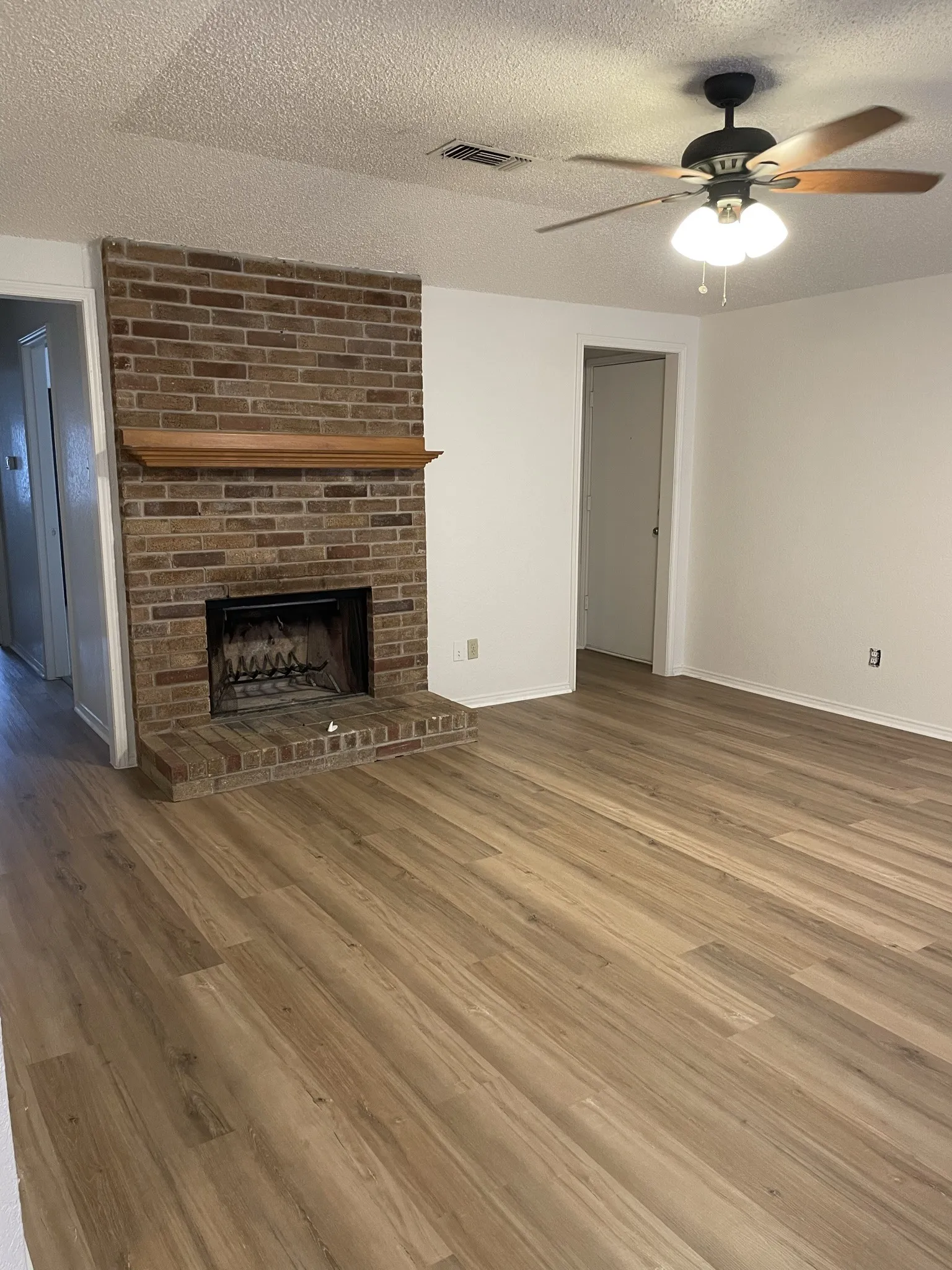 Brick fireplace with hearth, wood-finish flooring, ceiling fan with integrated lighting, and white wall finishes