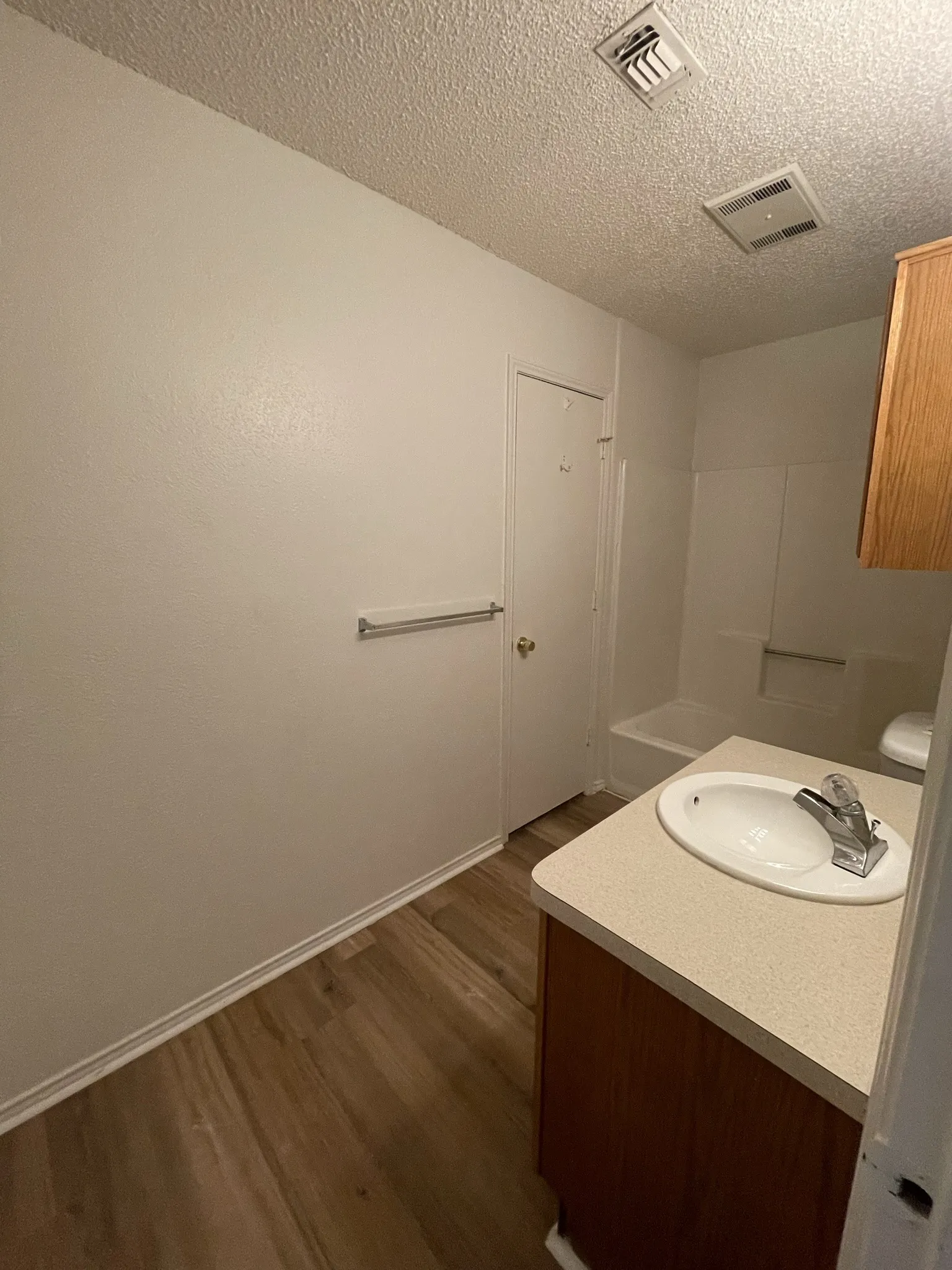 Bathroom featuring wood-finish flooring, a single vanity with an integrated sink, a built-in bathtub with shower surround, and a towel bar