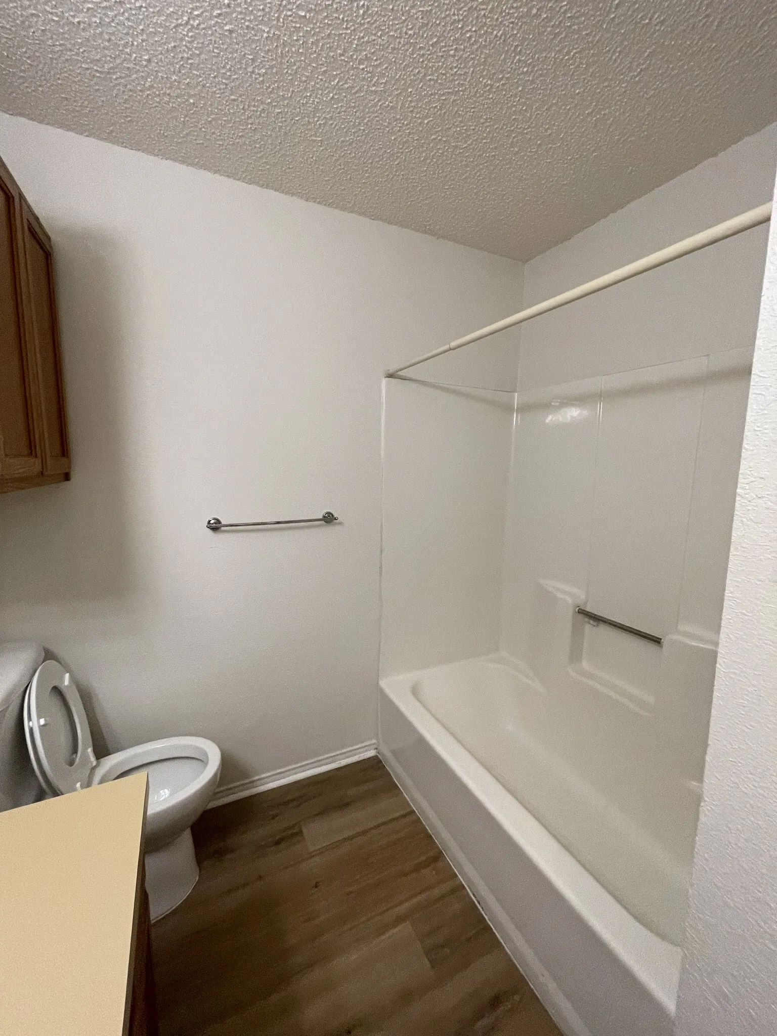 White bathtub with integrated shower, wood-finish flooring, and light-toned walls