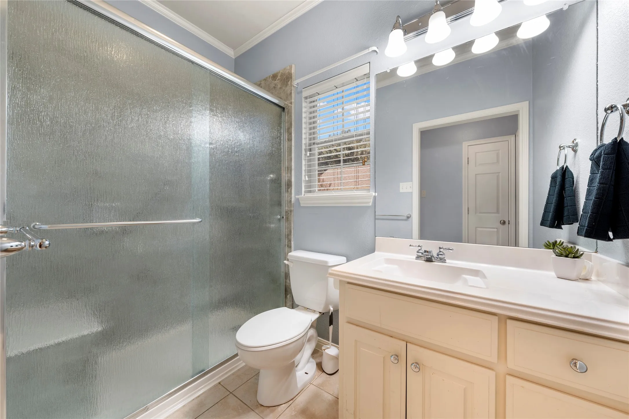 Frosted glass shower enclosure, single vanity with integrated sink, chrome fixtures, and a window with blinds