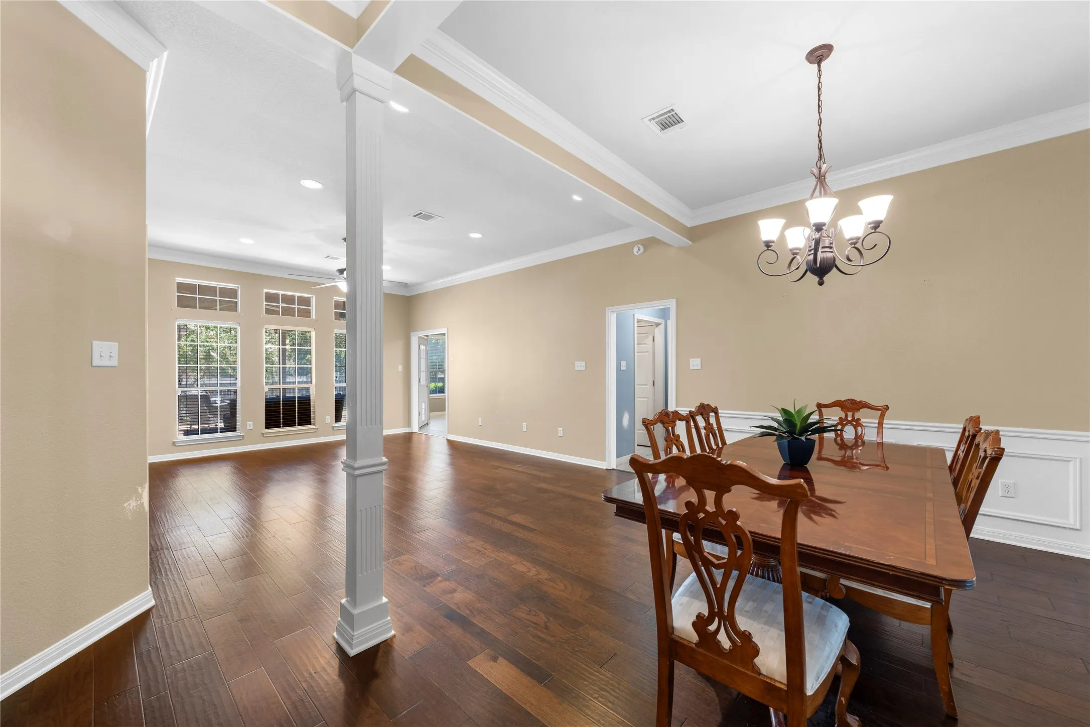 Elegant dining room showcasing rich wood-finish flooring, a coffered ceiling with recessed lighting, and a decorative chandelier