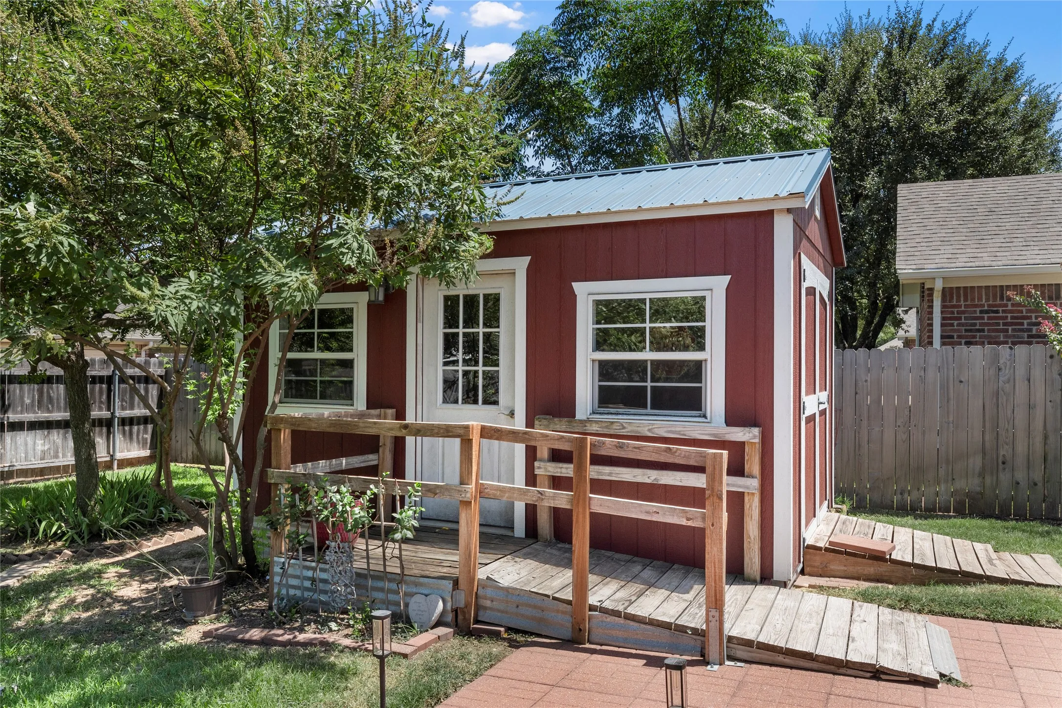 Red-sided shed with white trim, a corrugated metal roof, a wood-plank deck, and two wood-plank ramps
