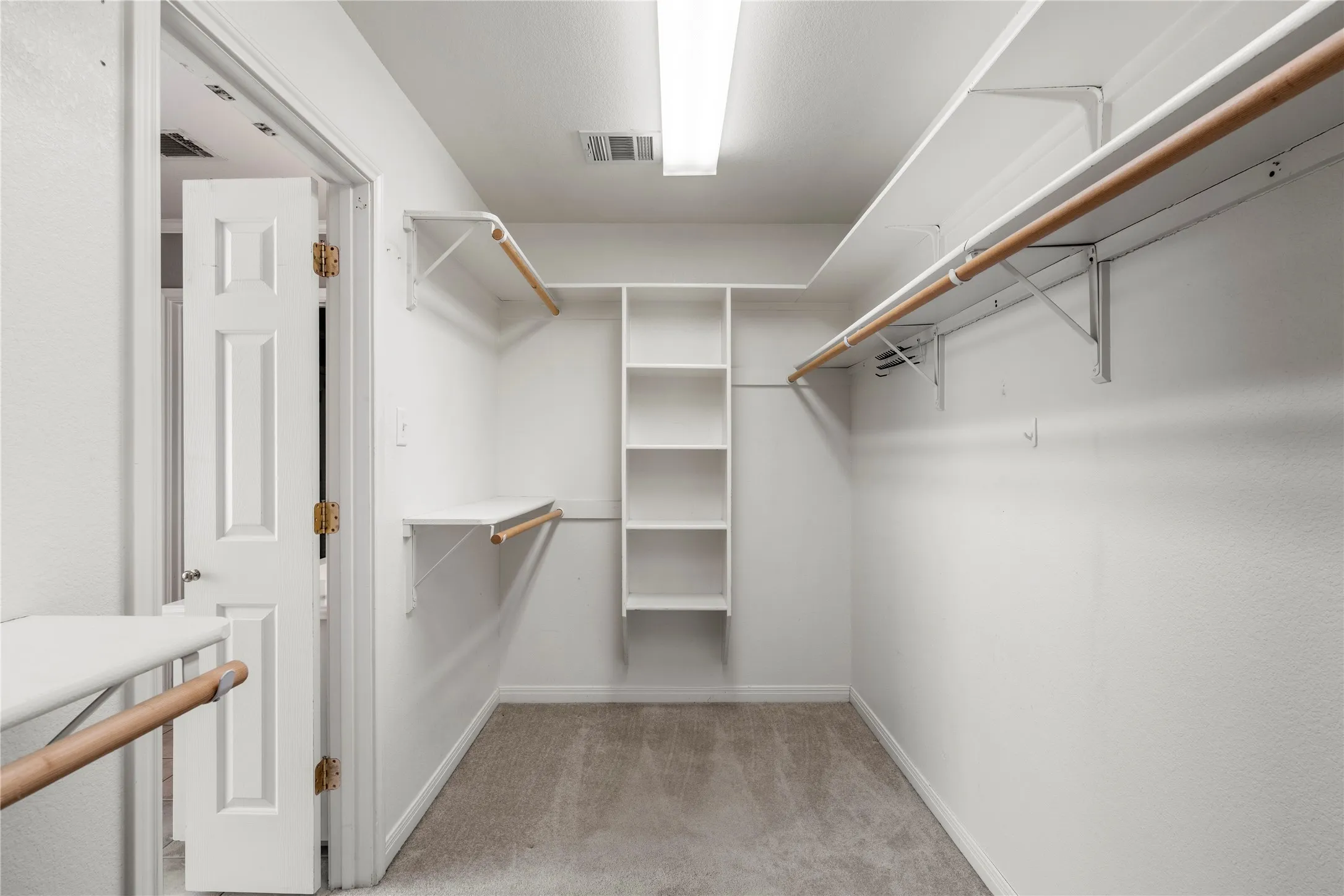 Walk-in closet featuring built-in shelving, multiple hanging rods, and carpet flooring