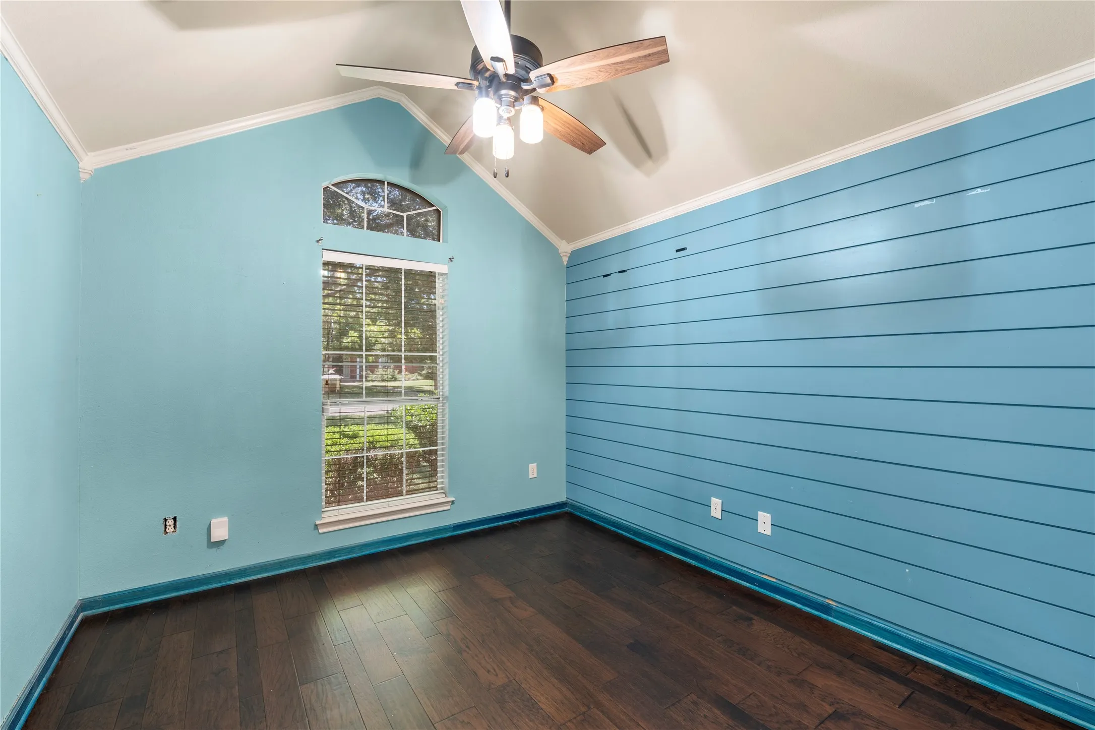 Vaulted ceiling with a ceiling fan, arched transom window, wood-finish flooring, and horizontal plank accent wall