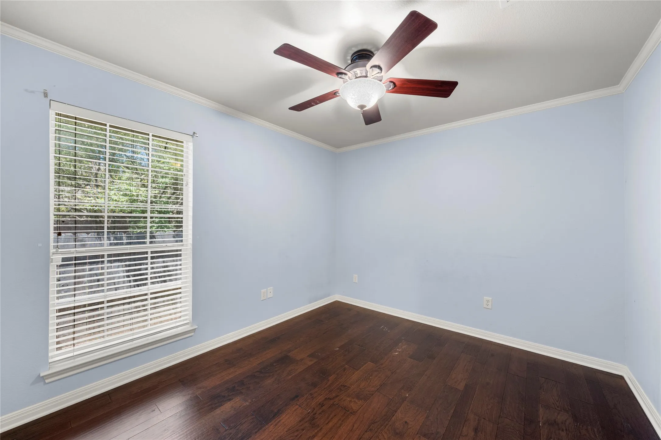 Window with blinds, wood-finish flooring, ceiling fan with light fixture, crown molding, and light-toned walls