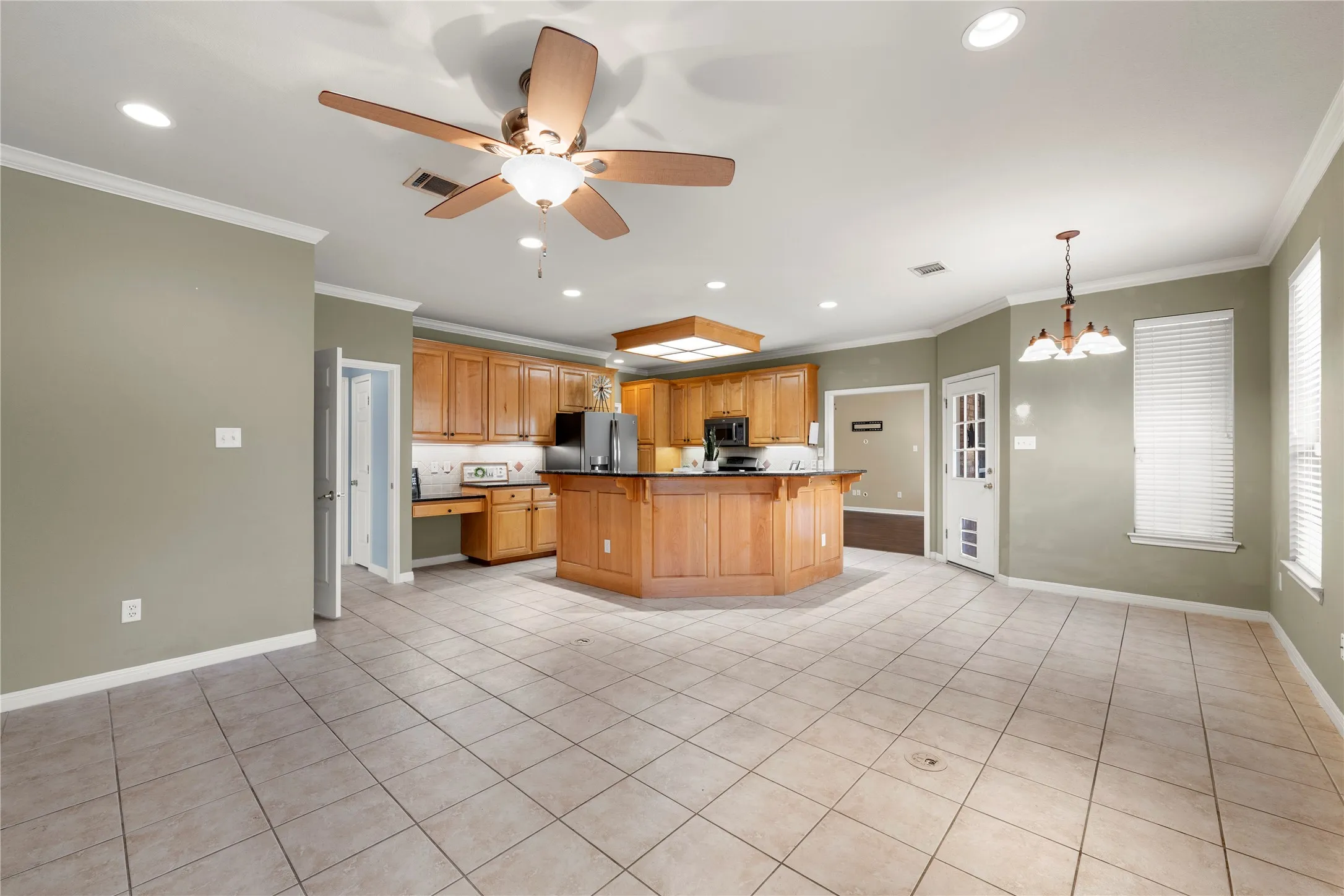 Spacious open-concept kitchen and dining area featuring wood cabinetry, stainless steel appliances, tile flooring, recessed lighting, and a ceiling fan with decorative drum shade