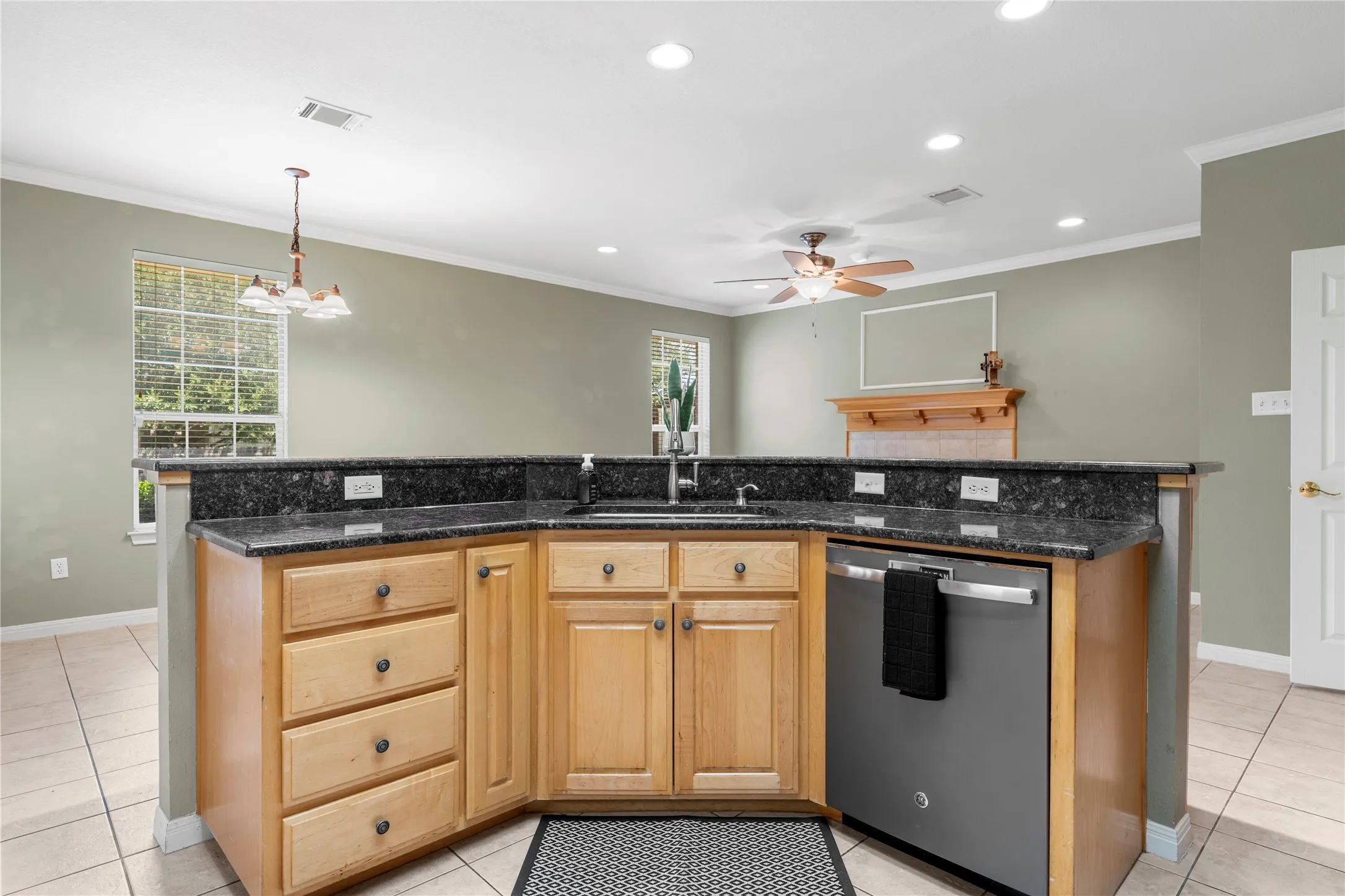 Kitchen with dark granite countertops, natural wood cabinetry, and stainless steel dishwasher