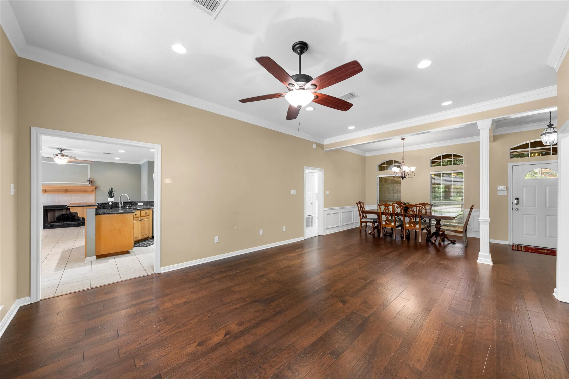 Spacious open-concept living area featuring rich wood-finish flooring throughout, recessed ceiling lighting, and a ceiling fan with integrated light fixture