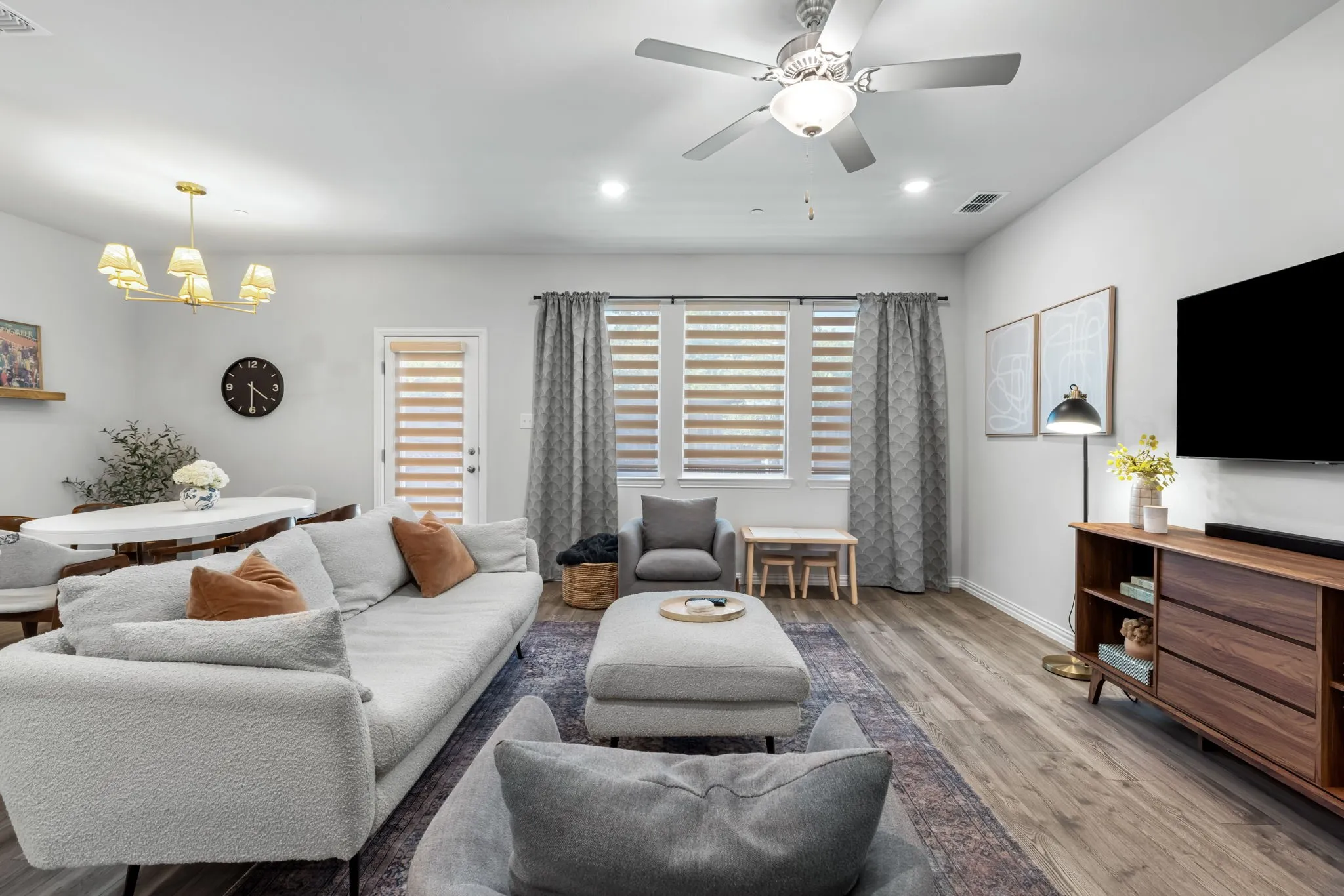 Bright, open living space featuring a light wood-finish floor, ceiling fan with integrated lighting, and wall-mounted flat-screen television