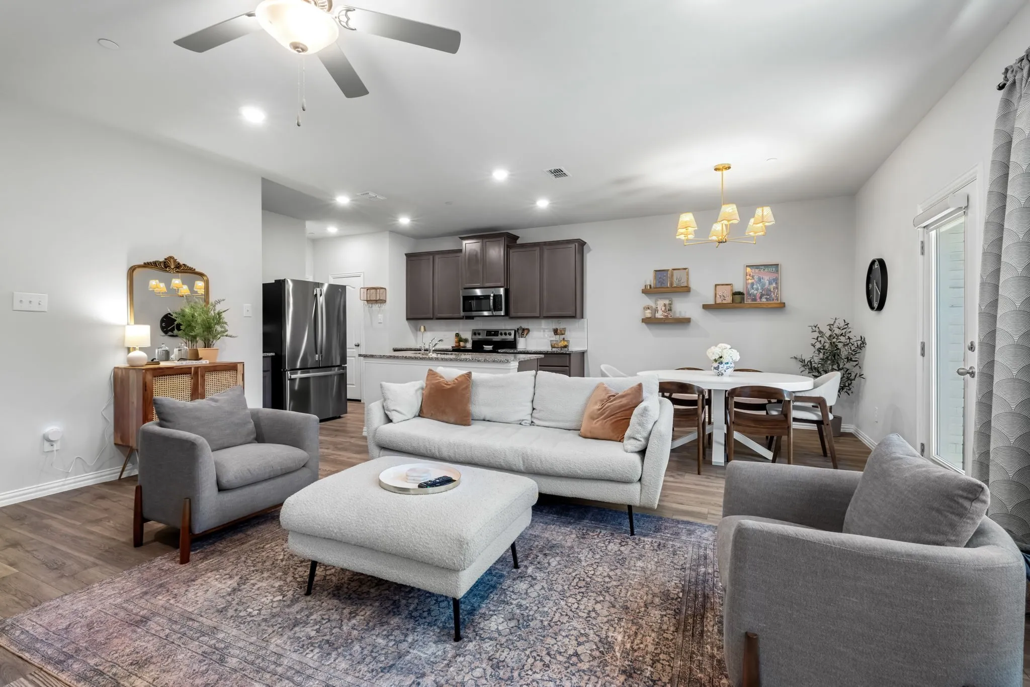 Open-concept living area featuring a light gray upholstered sofa, matching armchairs, and an ottoman with black metal legs atop a patterned area rug