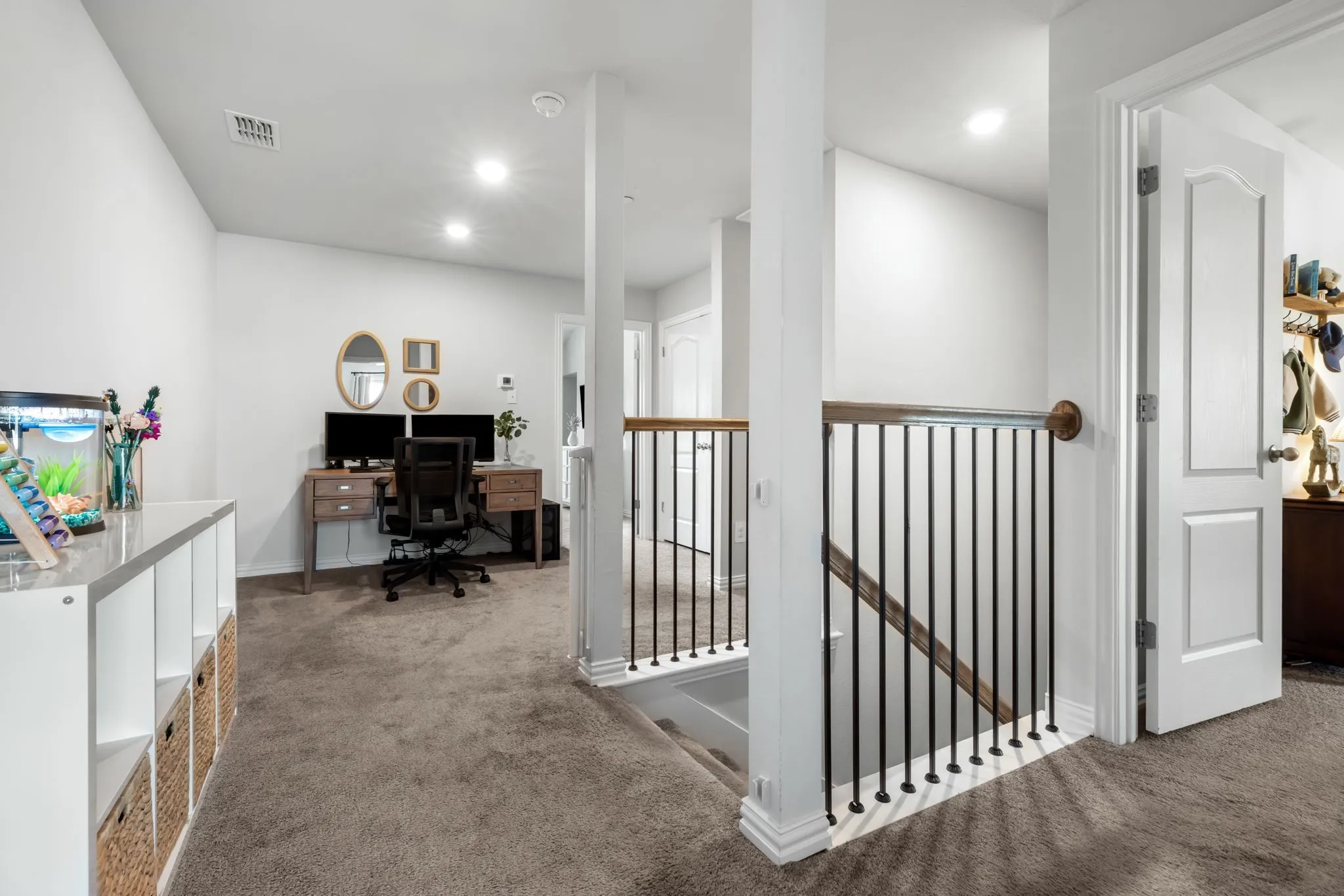Spacious upper-level landing featuring neutral carpet flooring, recessed lighting, white painted walls, and a black metal stair railing