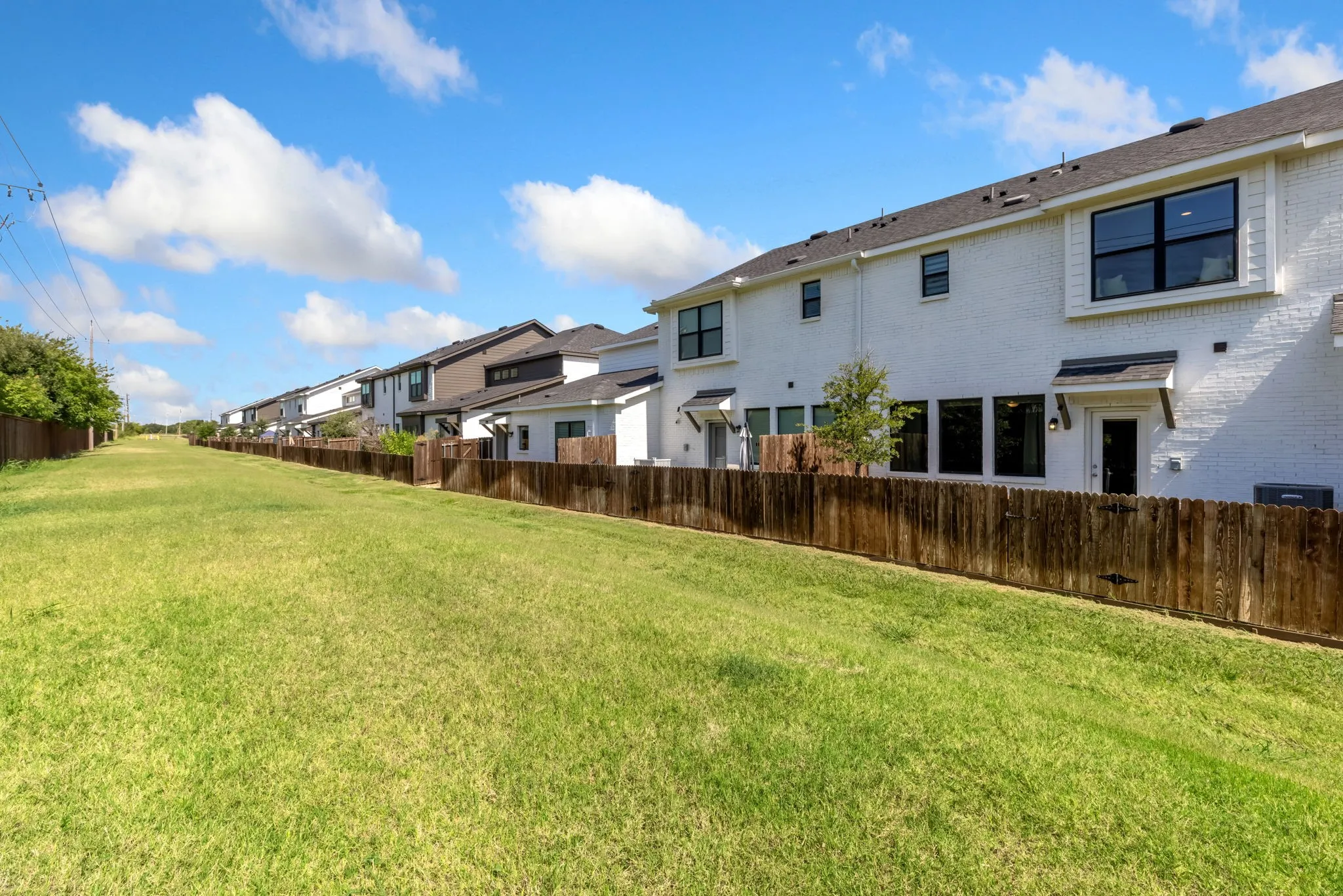 Expansive grassy area bordering multiple properties, featuring a privacy fence and contemporary building exteriors