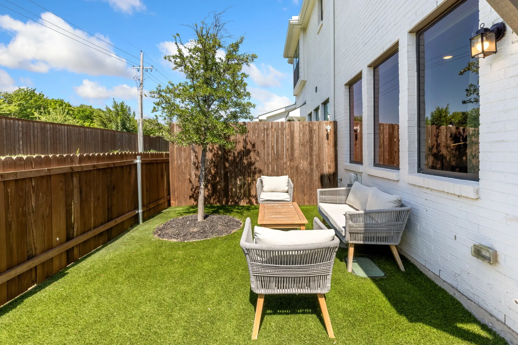 Private backyard retreat featuring manicured artificial turf, mature landscaping with specimen plantings, wooden privacy fencing, and multiple seating areas adjacent to the residence