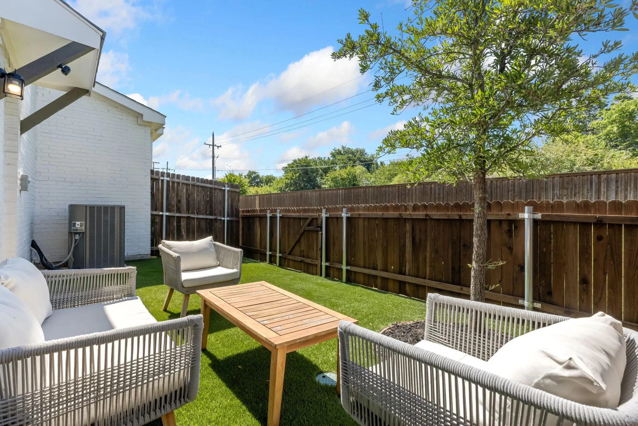 Private backyard area featuring artificial turf, a wood privacy fence, and a mature tree