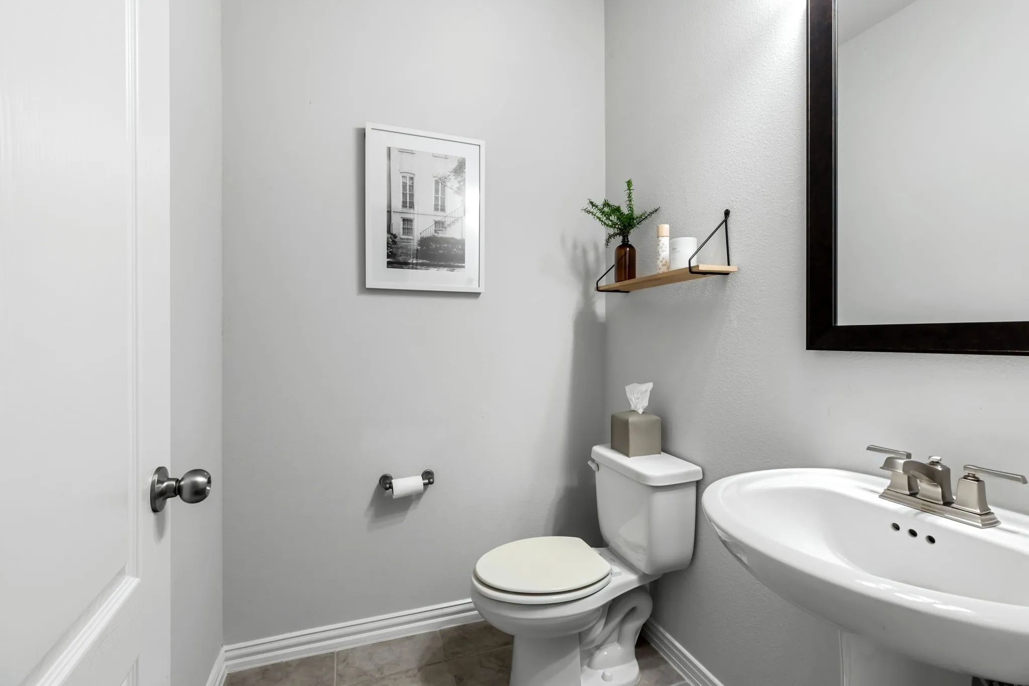 Pedestal sink with brushed nickel faucet, wall-mounted mirror with dark frame, white toilet, and light-toned wall paint