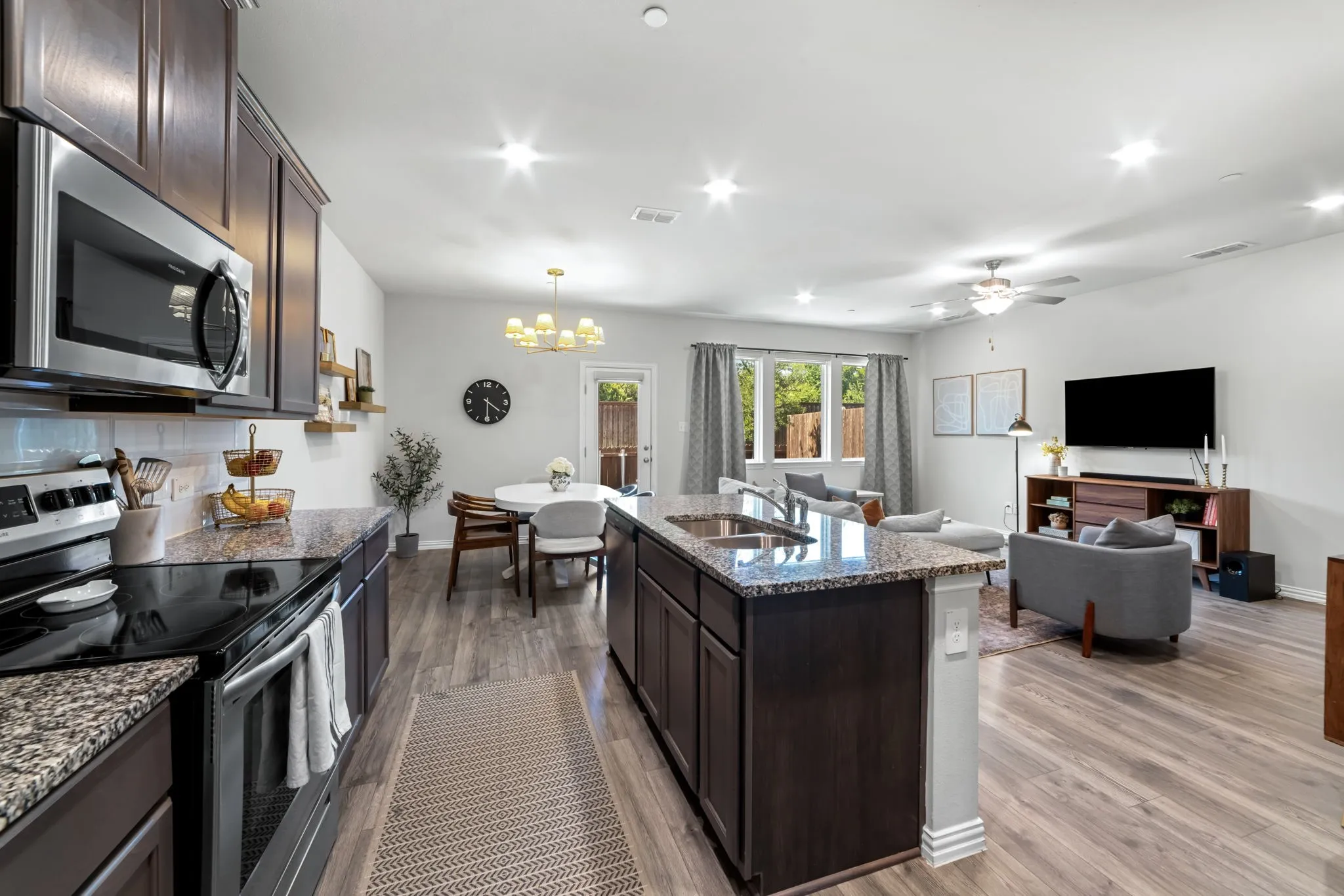 Open-concept kitchen and living area featuring a dark wood cabinetry island with a quartz countertop, stainless steel appliances including a microwave and range, granite countertops, and wood-finish flooring throughout