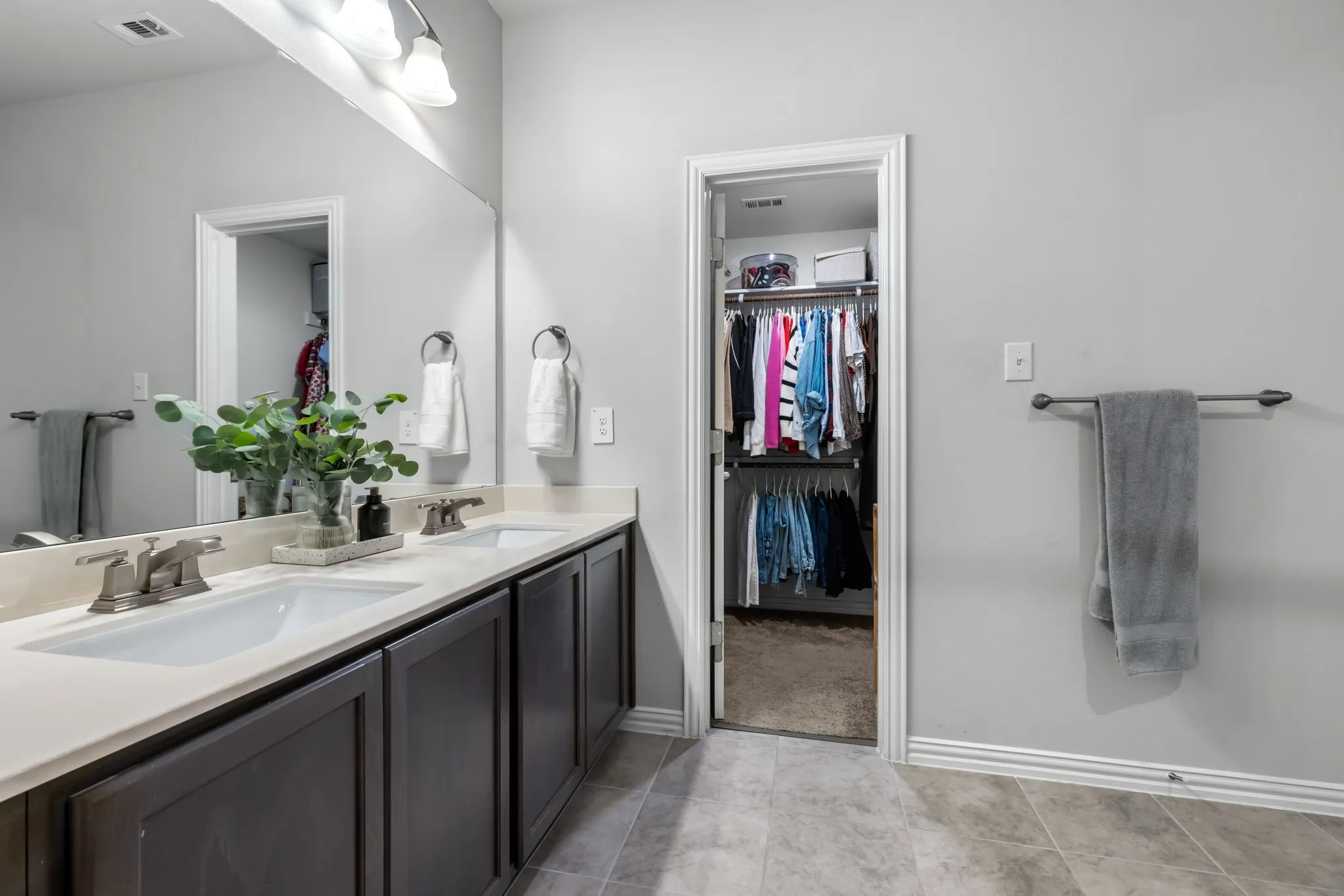 Dual sinks set in a light-toned countertop, dark wood-finish cabinetry, full-width mirror, brushed nickel fixtures, and tiled flooring