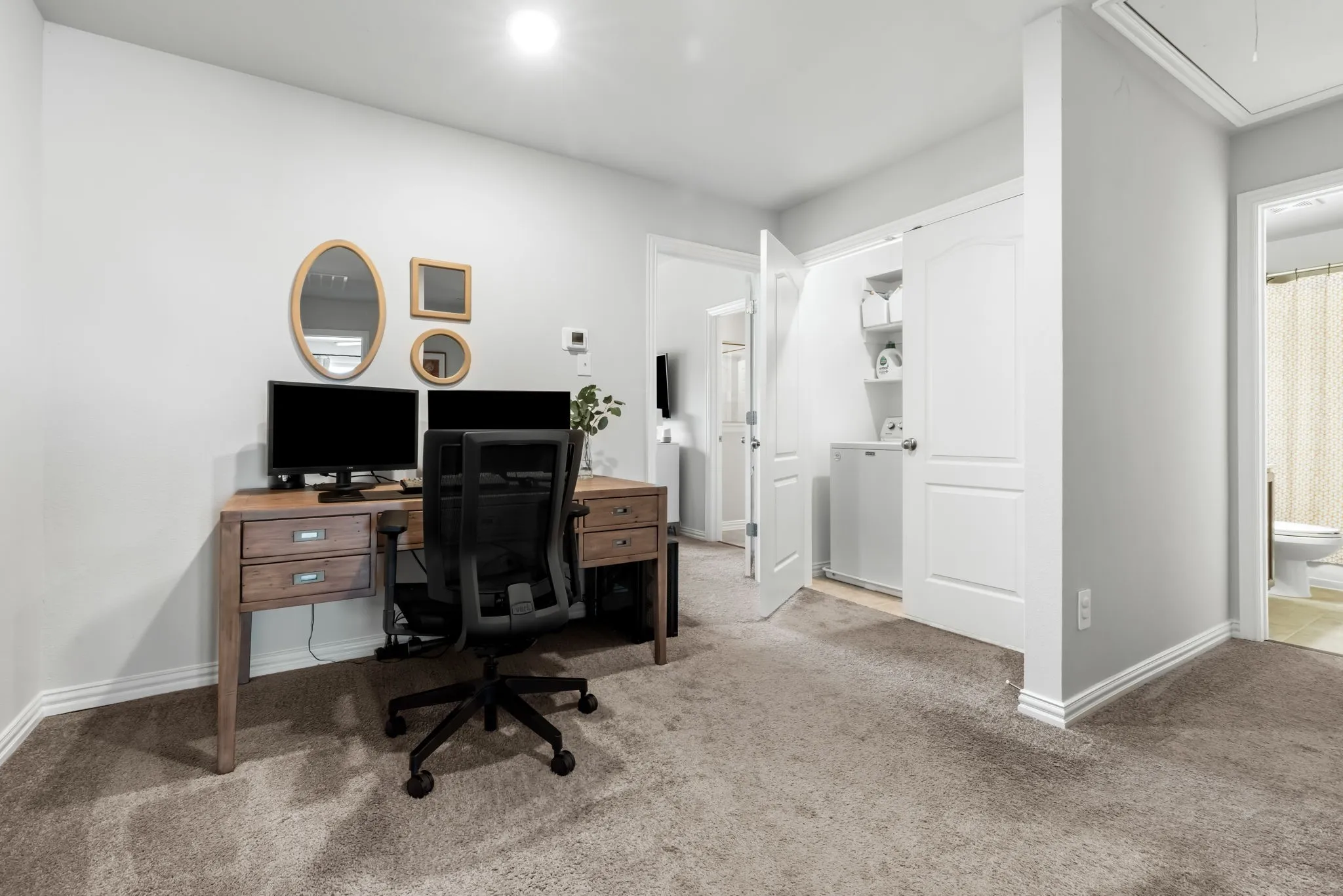 Dedicated home office featuring a wood-finish desk with multiple drawers, black ergonomic task chair, dual monitors, and abundant natural light