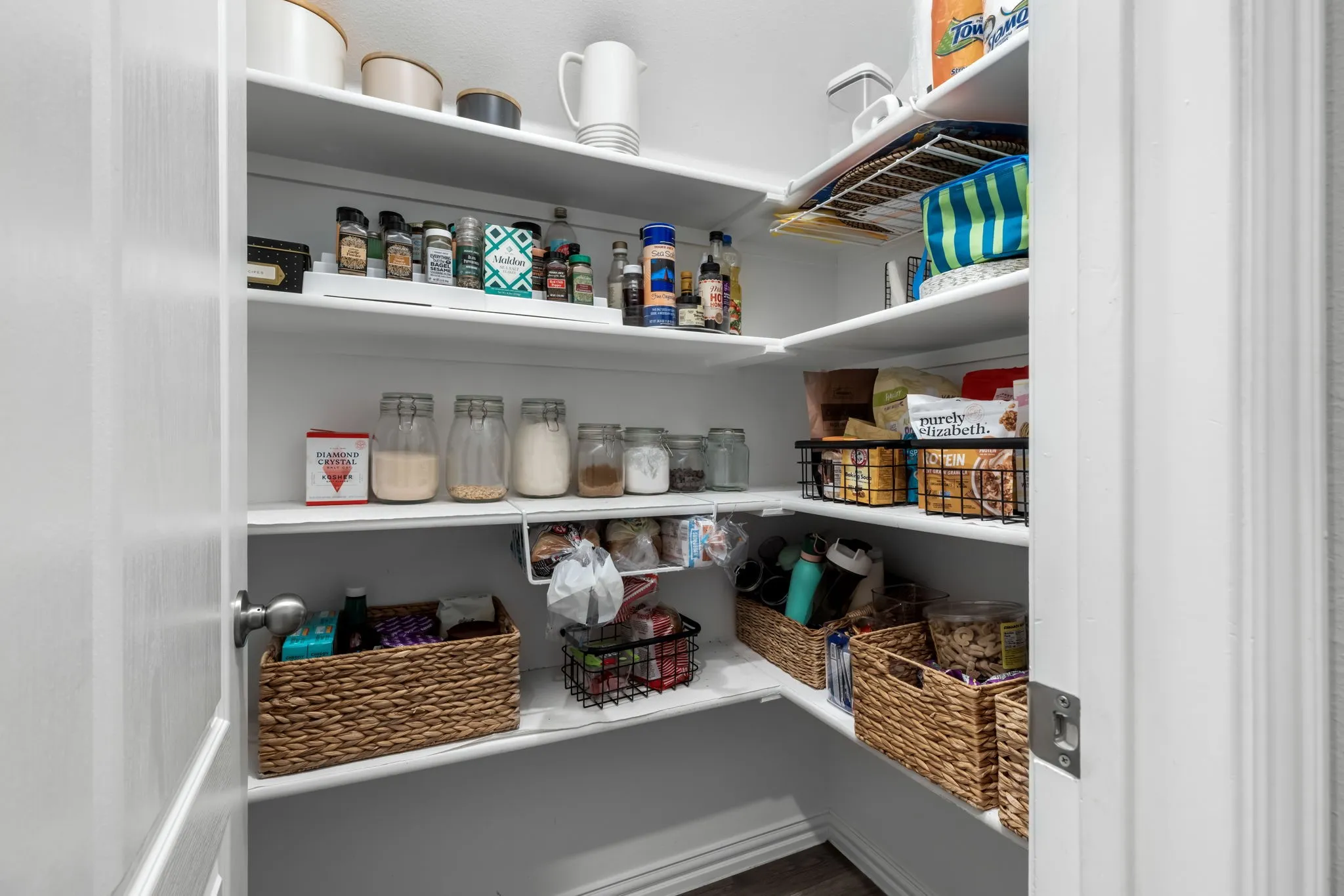Organized pantry featuring multiple shelves with ample storage capacity, woven baskets for containment, glass canisters and jars for dry goods, and dedicated space for pantry staples and household essentials
