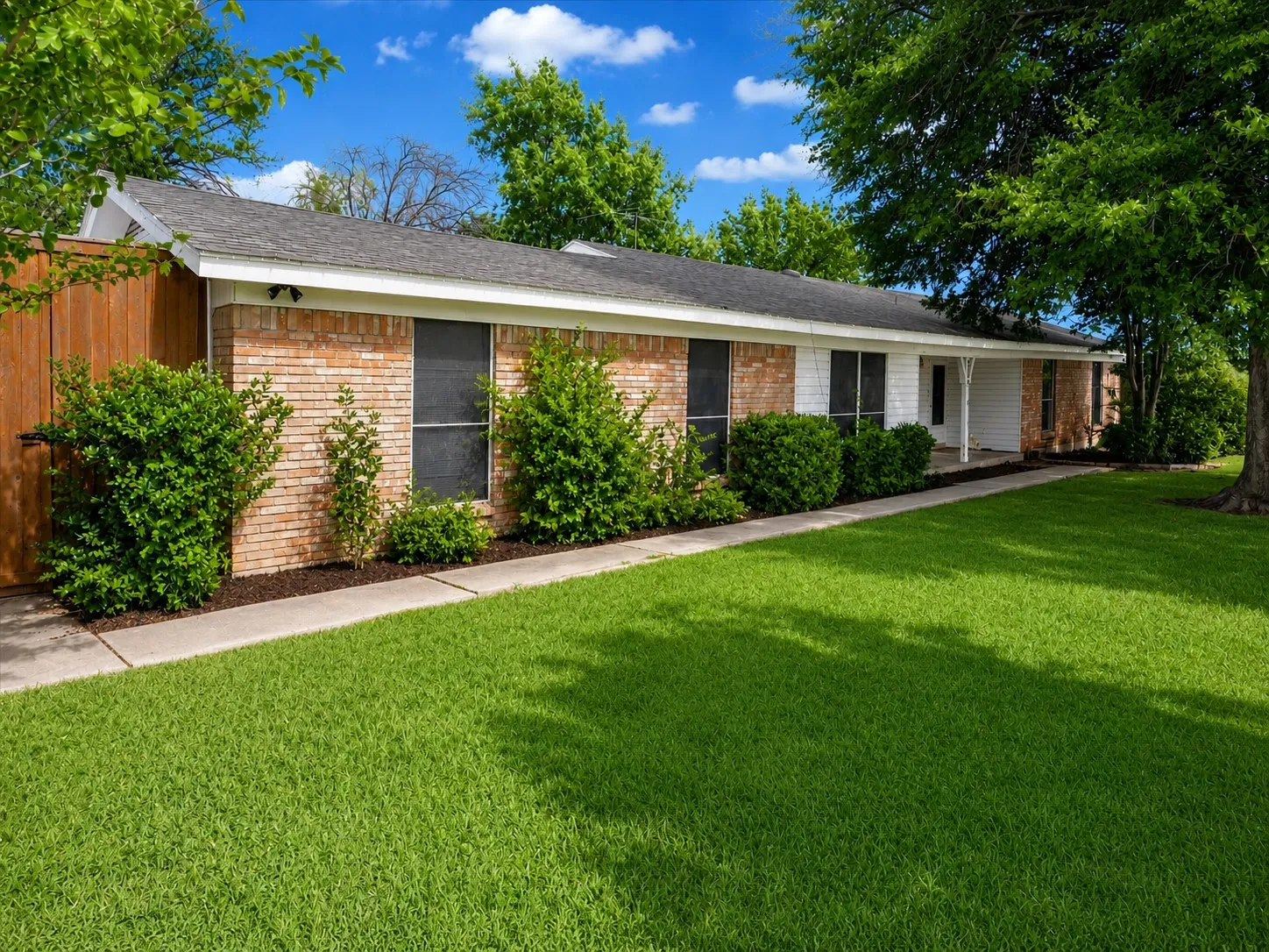 Brick and siding exterior with a covered entry, established landscaping, and a concrete walkway