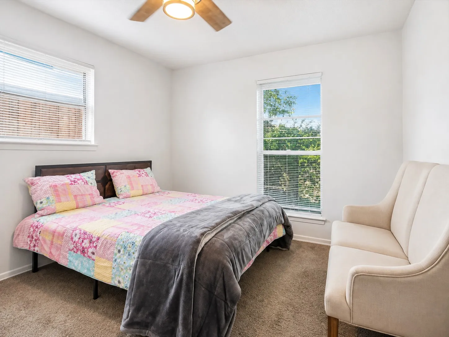 Bright room featuring a ceiling fan, two windows with blinds, and neutral carpeting