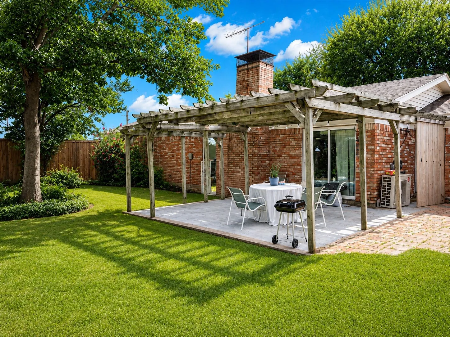 Brick residence with mature landscaping and expansive manicured lawn featuring a pergola-covered patio with brick hardscaping, outdoor dining area, and direct access to the home's interior spaces