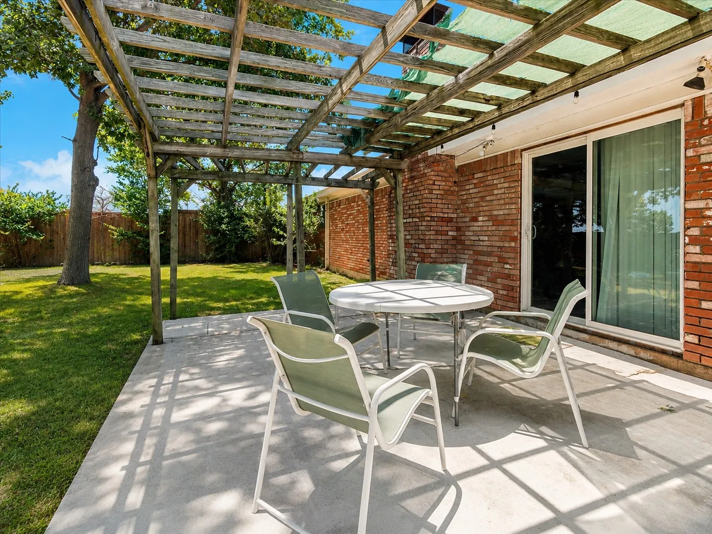 Spacious concrete patio with a wooden pergola structure and a sliding glass door entry to the interior