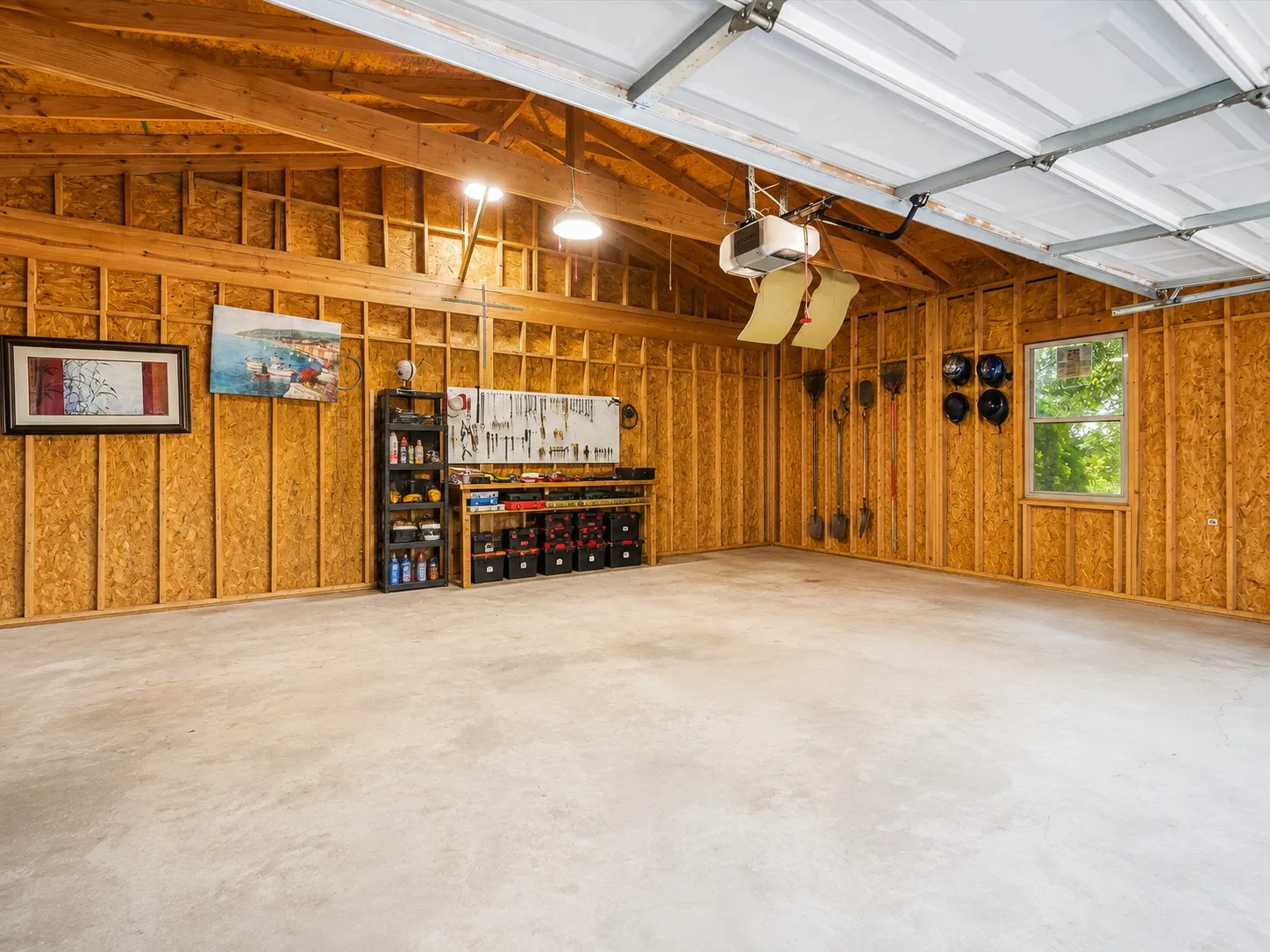 Spacious garage with wood-finish wall paneling, polished concrete flooring, recessed lighting, and built-in storage cabinetry