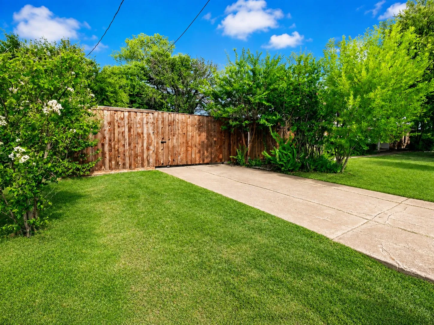 Expansive grassy lawn, mature trees, and a tall wood plank fence with a gate