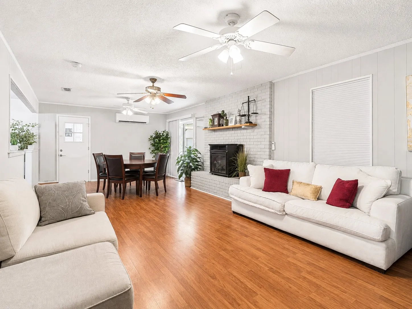 Wood-finish flooring throughout, white painted brick fireplace with wood mantel, and multiple ceiling fans