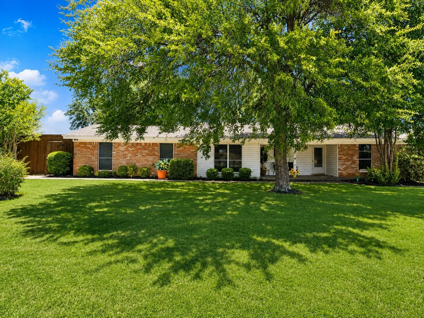 Spacious brick and stucco residence with mature shade trees casting dappled light across the manicured lawn