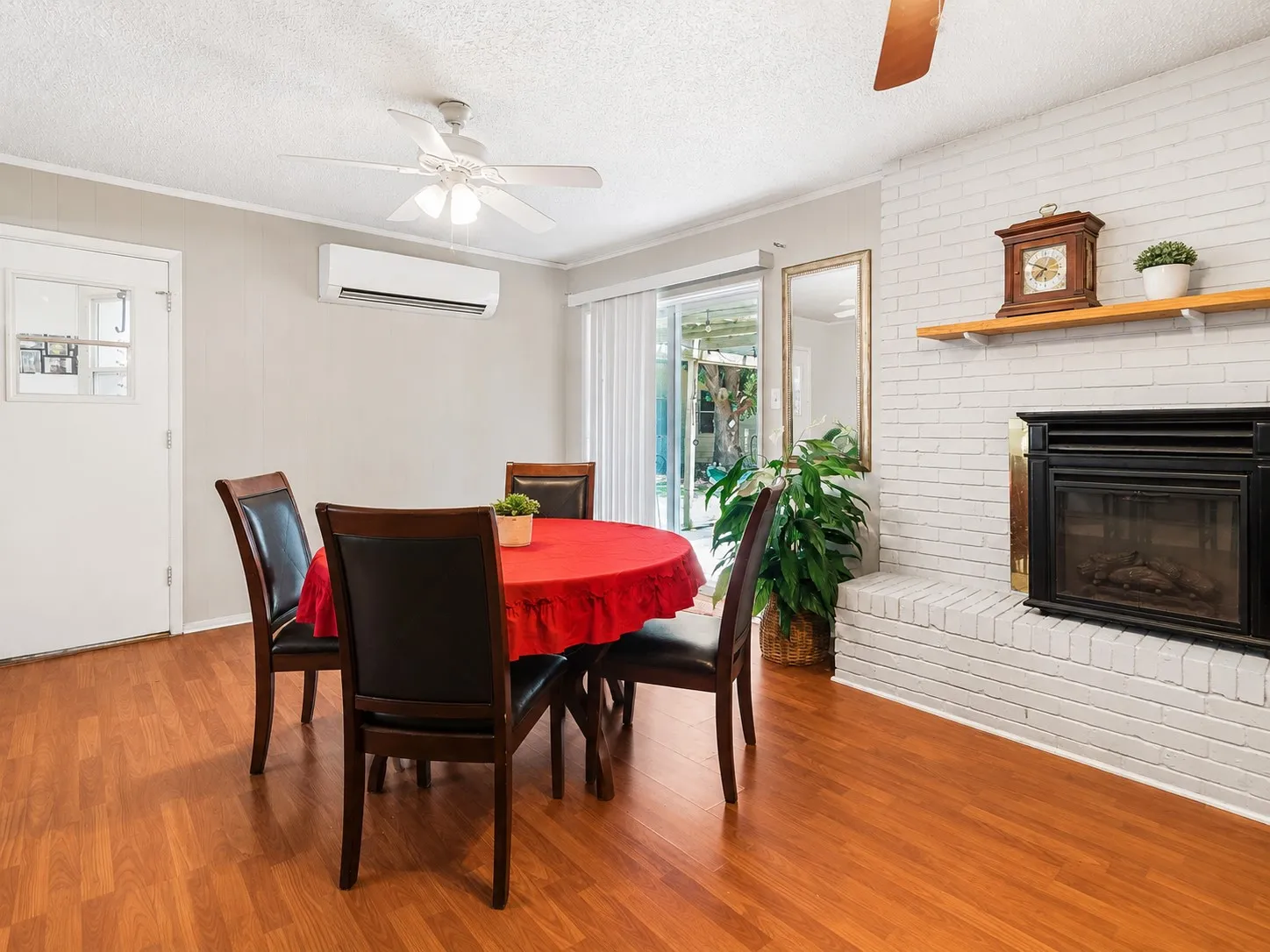Wood-finish flooring, white brick fireplace, sliding glass door, ceiling fan, and wall-mounted air conditioning unit
