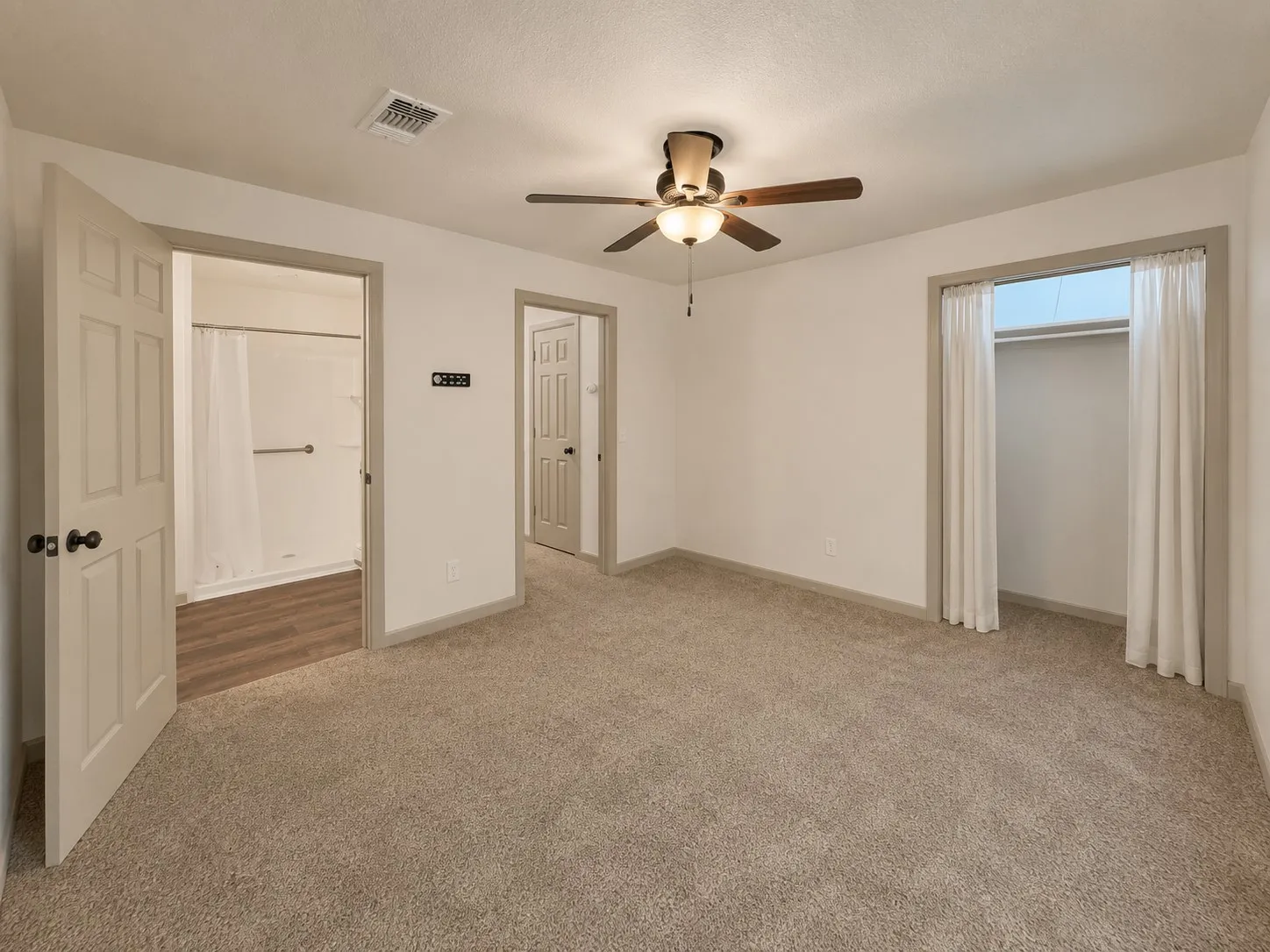 Carpeted room featuring a ceiling fan with integrated lighting, a built-in closet with curtain closure, and access to a bathroom with wood-finish flooring and a shower-tub combination
