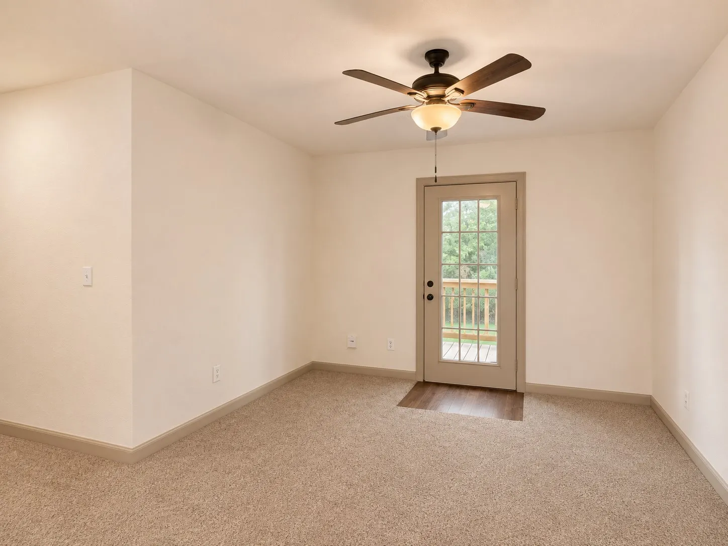 Neutral tone walls with coordinating trim, soft carpeting, built-in ceiling fan with light fixture, and a glass-paneled door leading to an outdoor deck