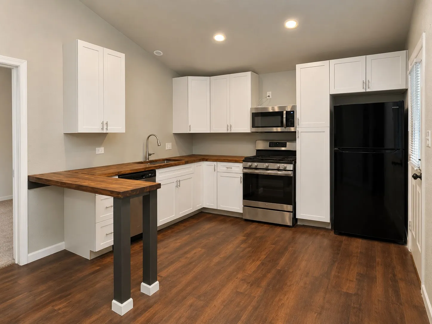 Modern kitchen featuring wood-finish flooring, white cabinetry, wood-finish countertops, stainless steel appliances, and recessed lighting