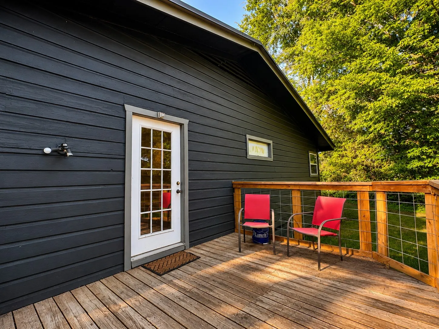 Dark-toned horizontal siding with white trim, wood-plank deck, and a wood railing with wire infill
