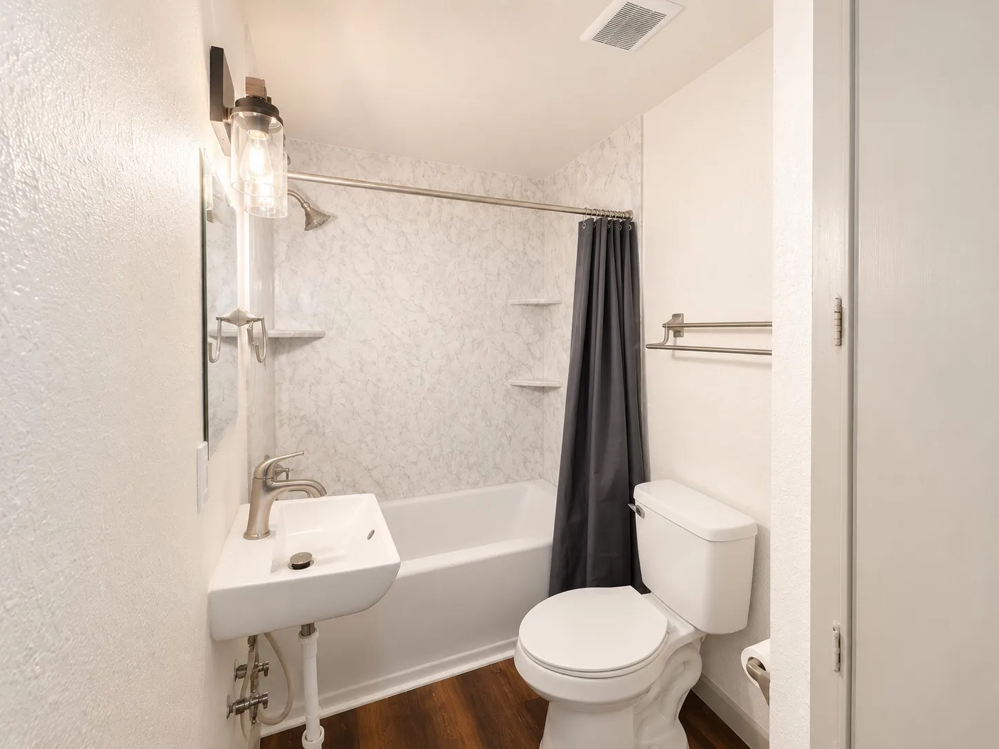 Bathroom featuring wood-finish flooring, a white corner sink, and a modern vanity light fixture