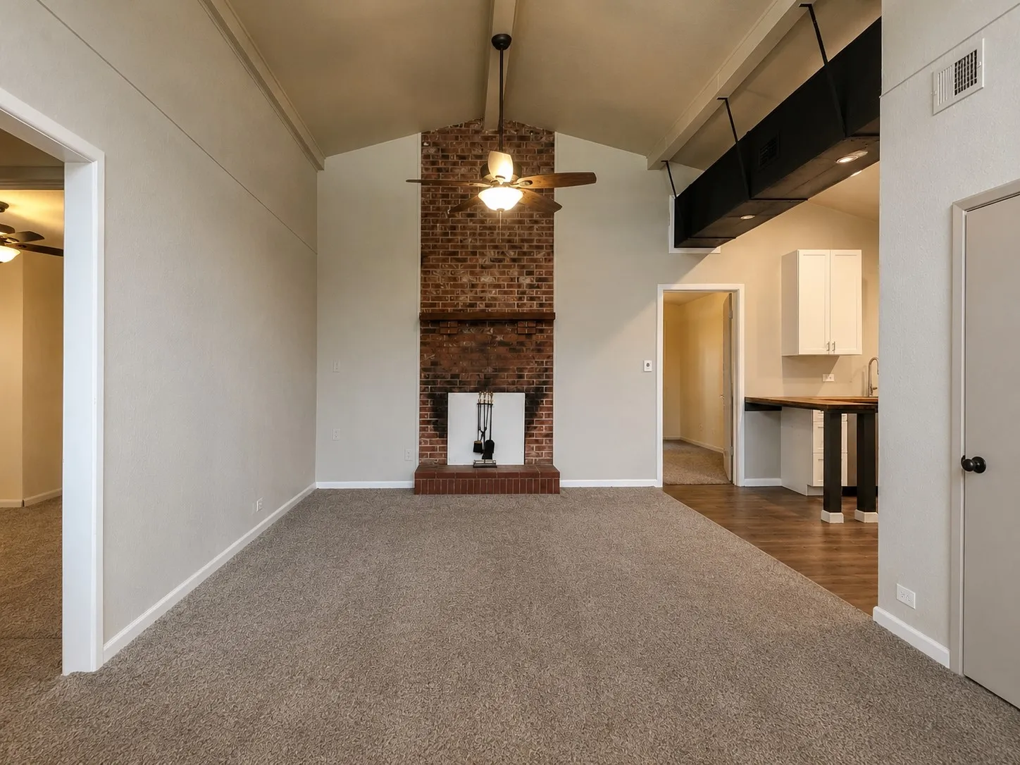 Vaulted ceiling, brick fireplace with hearth, ceiling fan, carpet flooring, and wood-finish flooring