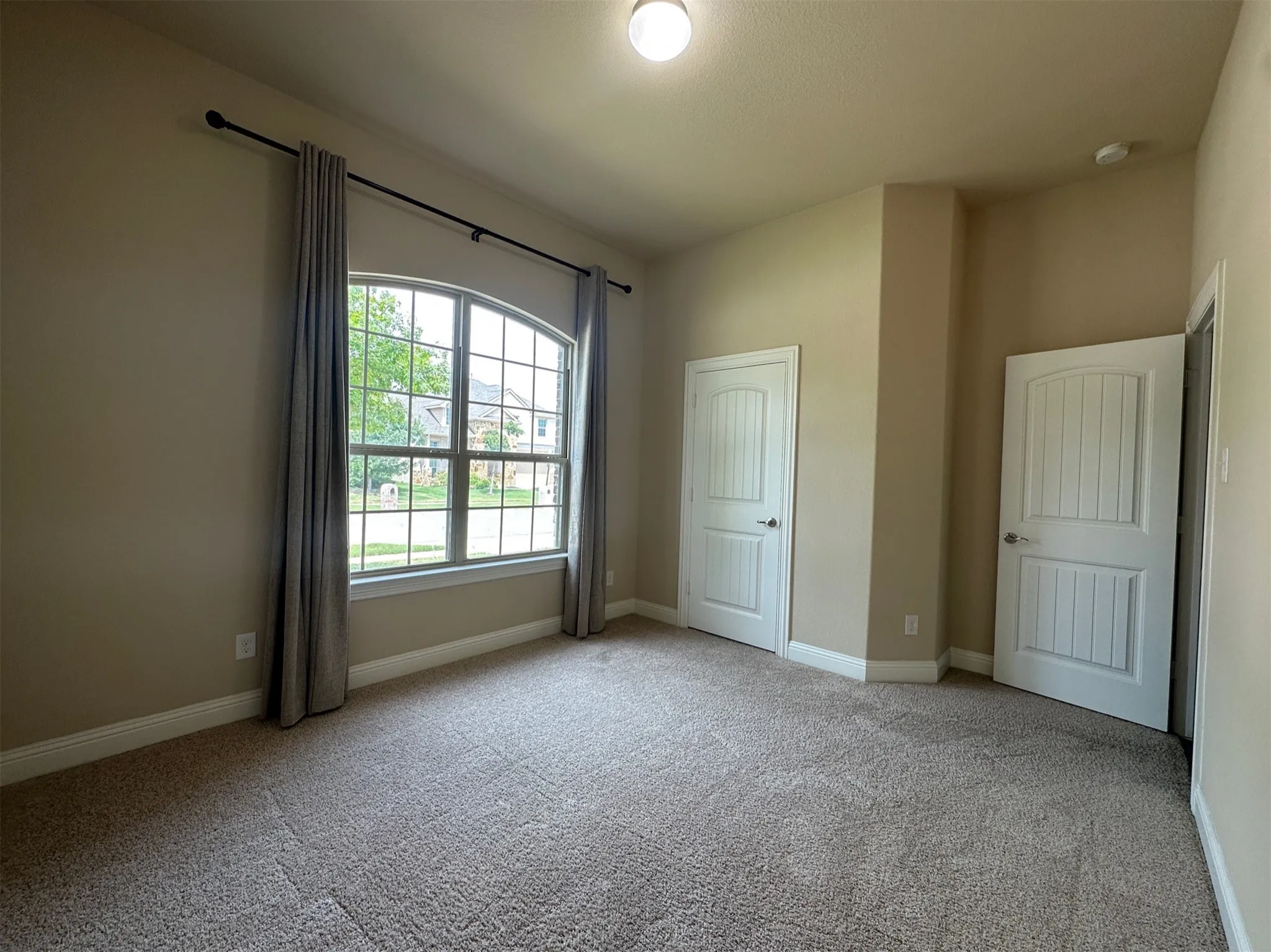 Spacious room featuring an arched window, neutral carpeting, and two paneled interior doors