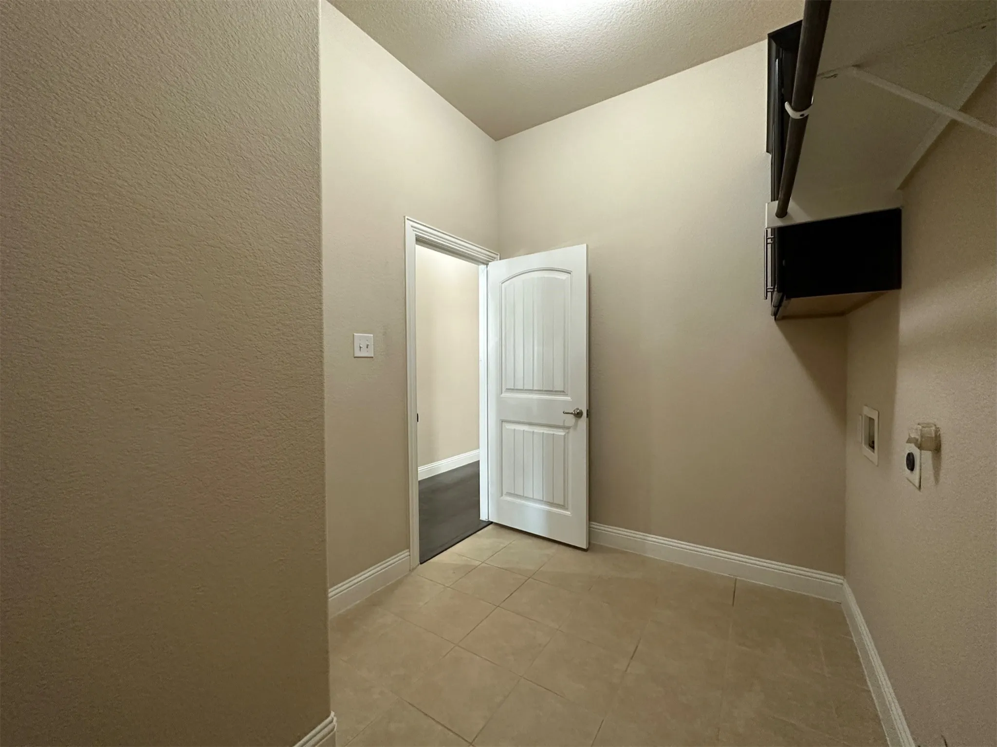 Utility room featuring neutral wall tones, tile flooring, and integrated shelving with a hanging rod