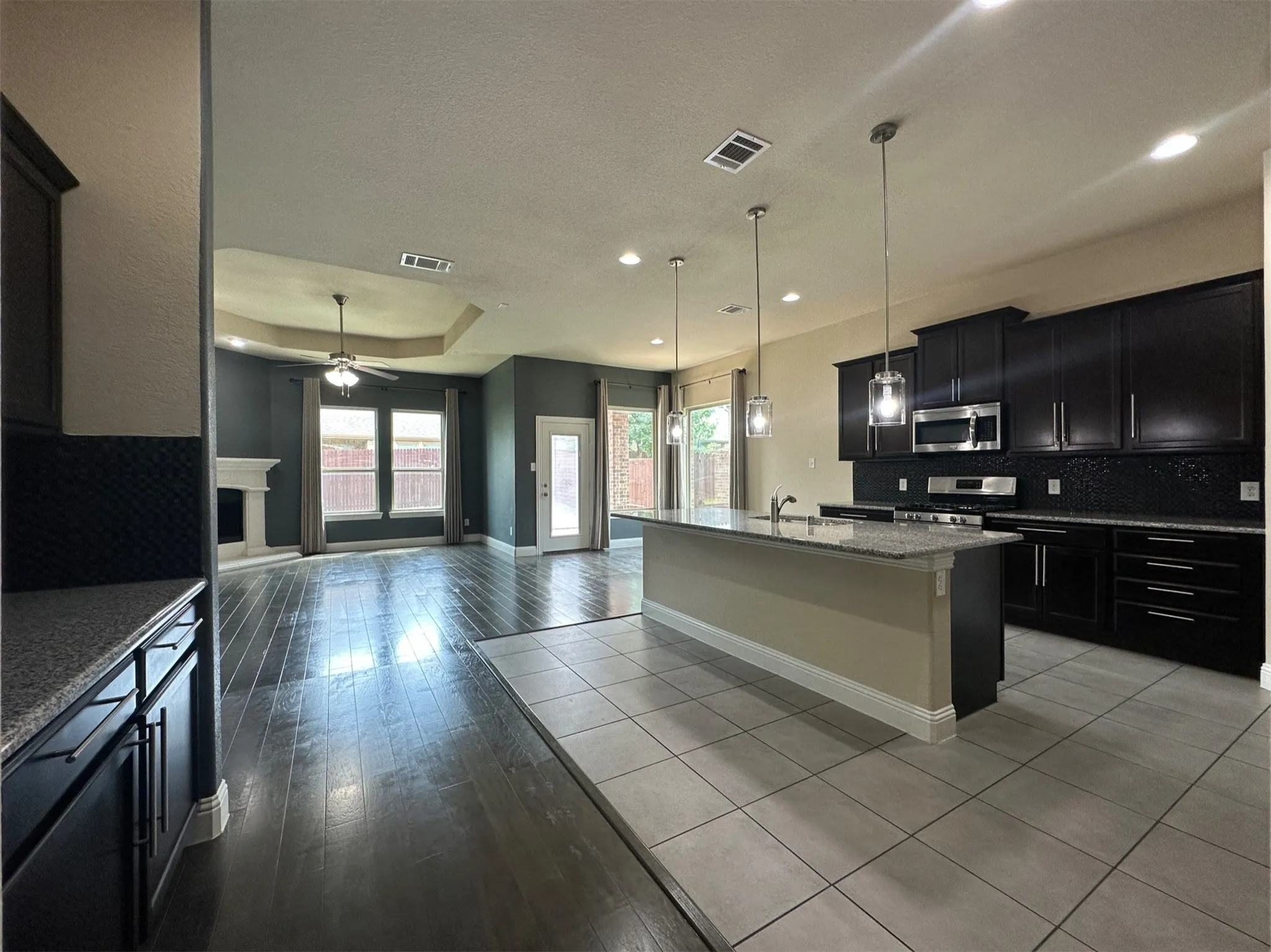 Open-concept living space featuring a spacious kitchen island, dark wood-finish flooring, a tray ceiling, and a fireplace with a white mantel